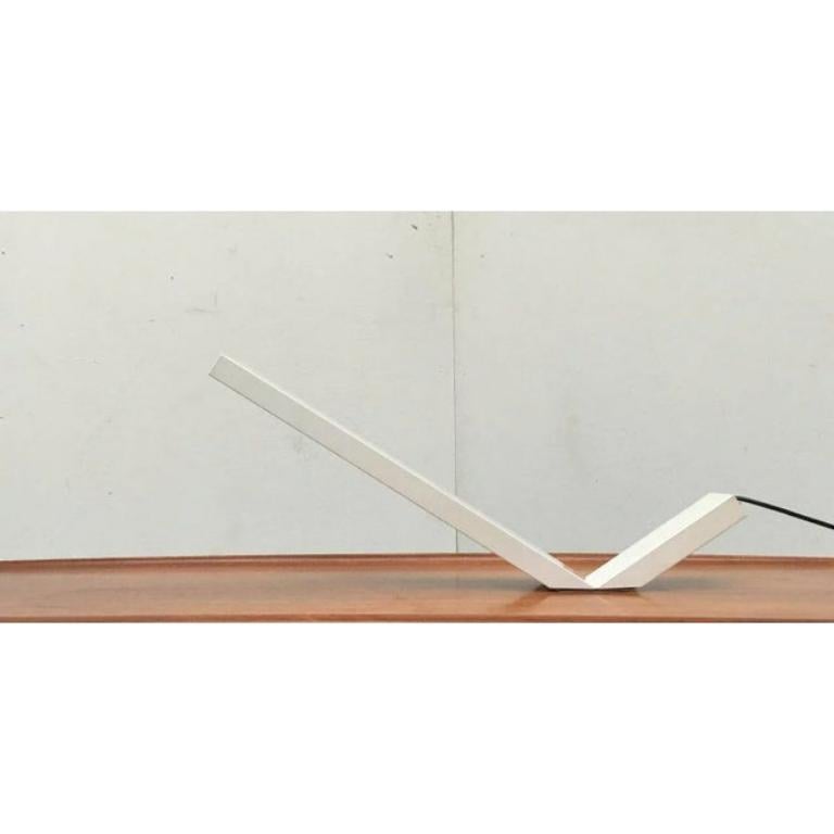 Rara lampada da tavolo del produttore italiano Eleusi basata su un disegno di Marco Zotta degli anni '80.

La forma di questa lampada segue un gesto eclatante. Un angolo piatto, con due gambe di lunghezza diversa, che si riduce quasi a zero