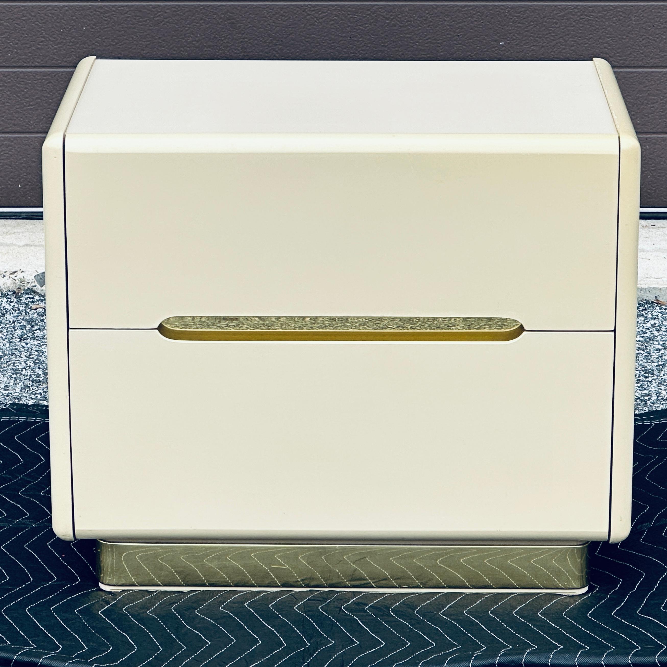 Vintage 1980’s Lane nightstand in cream-colored lacquer with striking brass banding accent. Substantial in presence yet minimalistic and modern in design, this piece makes a statement. The polished, shiny brass banding on base (front and sides) and