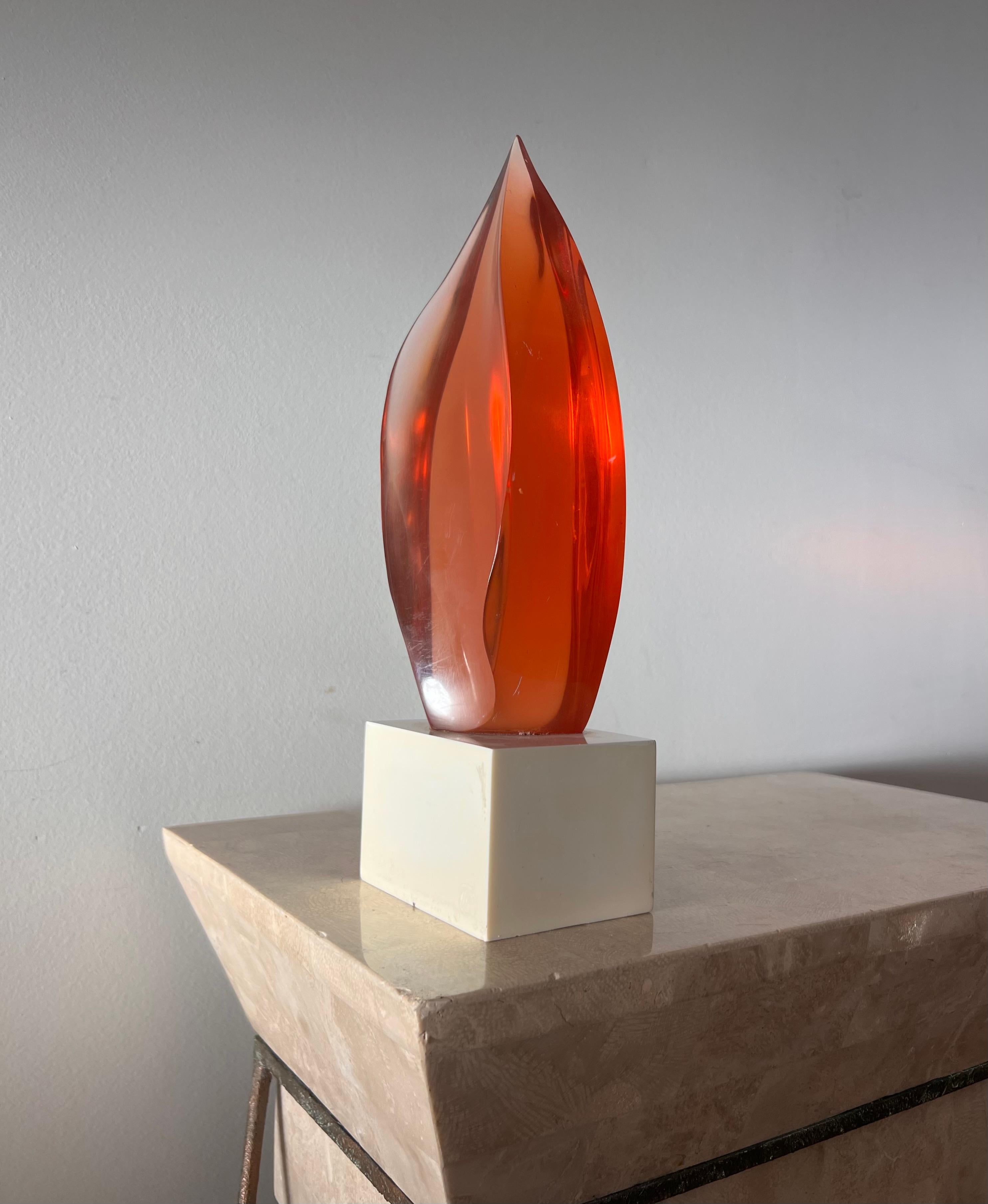A vintage postmodern lucite sculpture of a fire’s flame, mounted on plinth, 1983. One side of the plinth has been engraved with a dedication to “Dr. Bob” - please see the photos. The flame itself is brilliant iridescent coral orange hue which casts