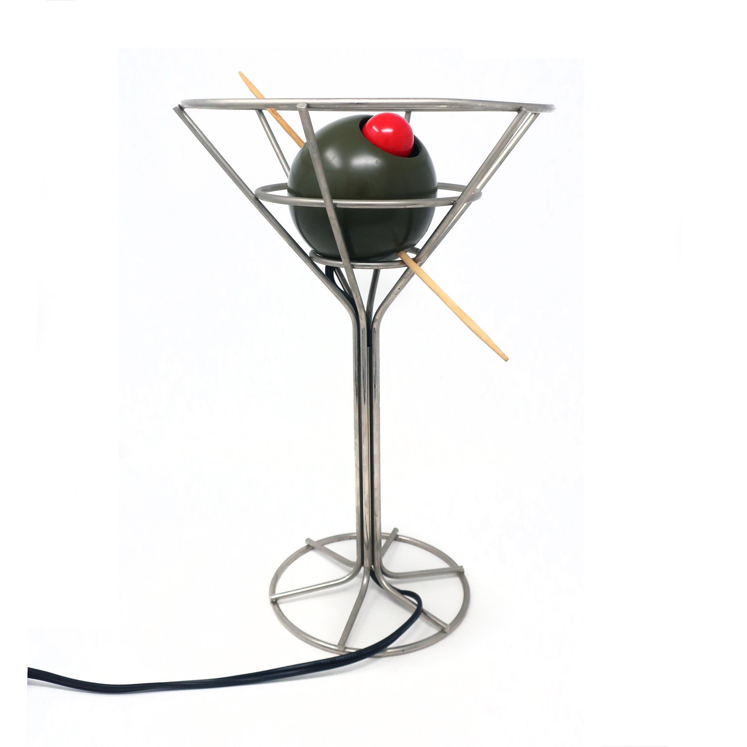 Una rara lámpara de martini postmoderna de 1993 diseñada por David Krys. El alambre metálico da forma al vaso con una aceituna verde ensartada rellena de una bombilla roja disfrazada de pimiento. Ideal para los amantes del arte pop, los utensilios