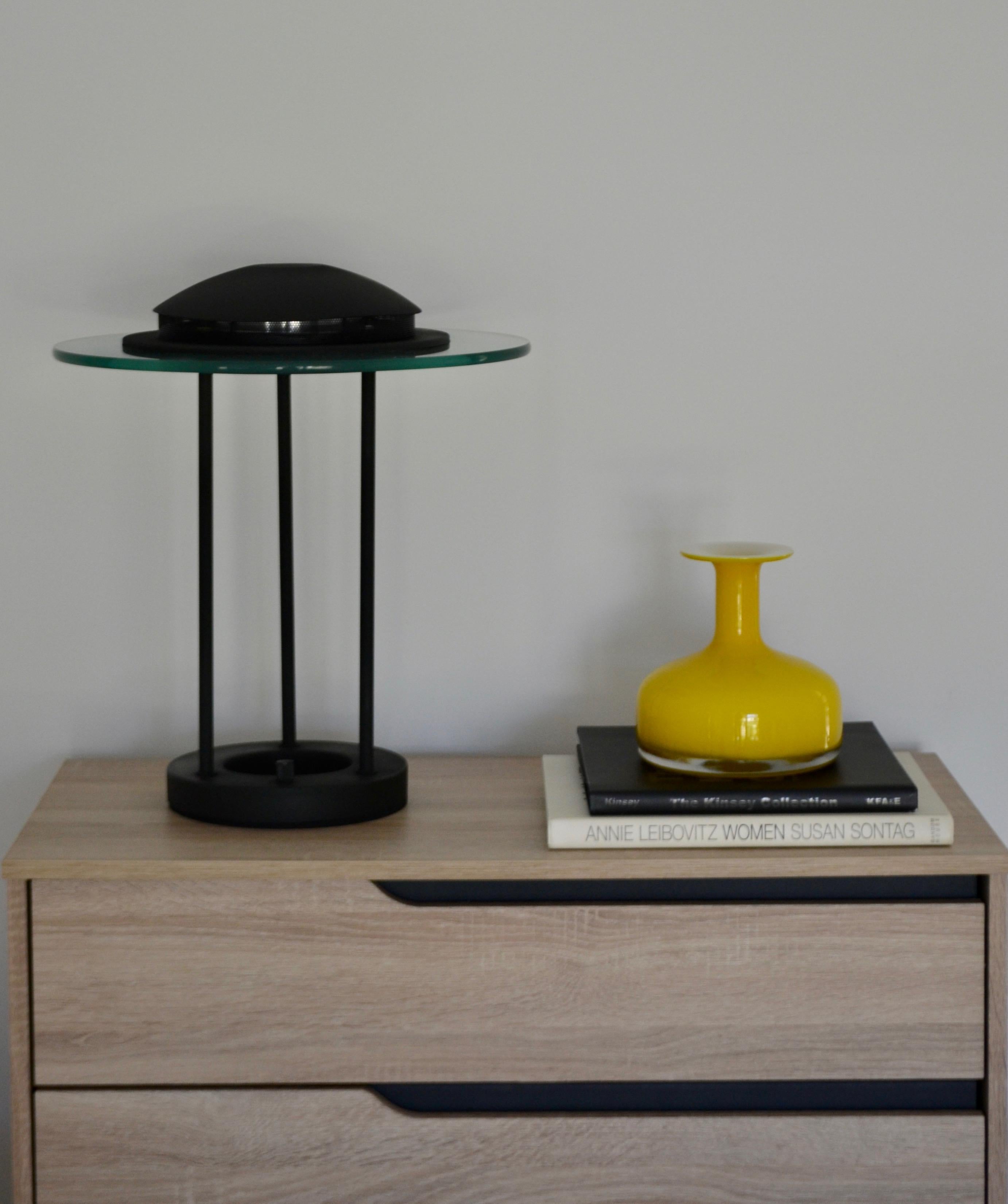 Striking Postmodern matte black table lamp, circa 1980s. This sculptural lamp is designed of lacquered metal with a sleek glass disc integrated into the dome-shaped top of the form. Dimmable halogen lightbulb.
Measurements: 18.5
