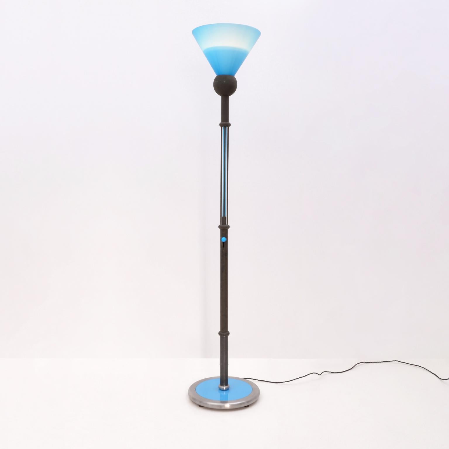 Postmodern Memphis style torchiere/ floor lamp, Italy c. 1980. The rough burnished metal lamp rod has the typical Memphis 'Pilastro' composition, with a glass tube segment and a glass light switch insertion. The blue with white inlay conical glass