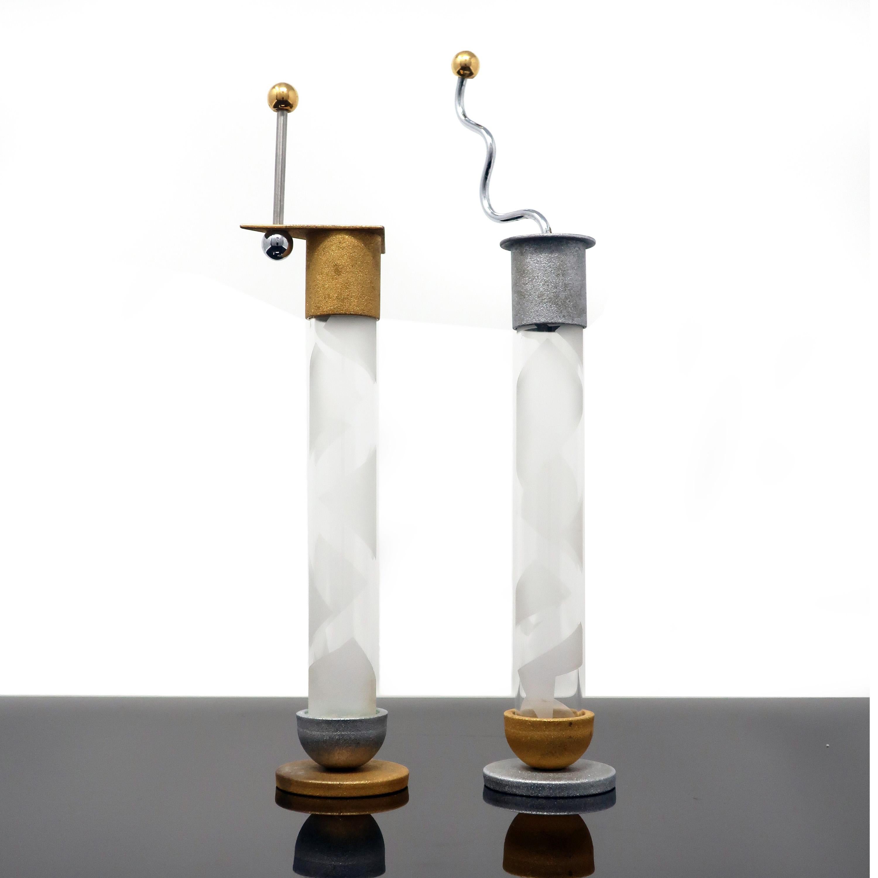 An eye-catching set of postmodern salt and pepper shakers by Vermont metalsmith Bruce R. MacDonald. Gold and silver colored bases and tops with etched glasses cylinders to hold the salt and pepper. These slender vessels are capped with primary