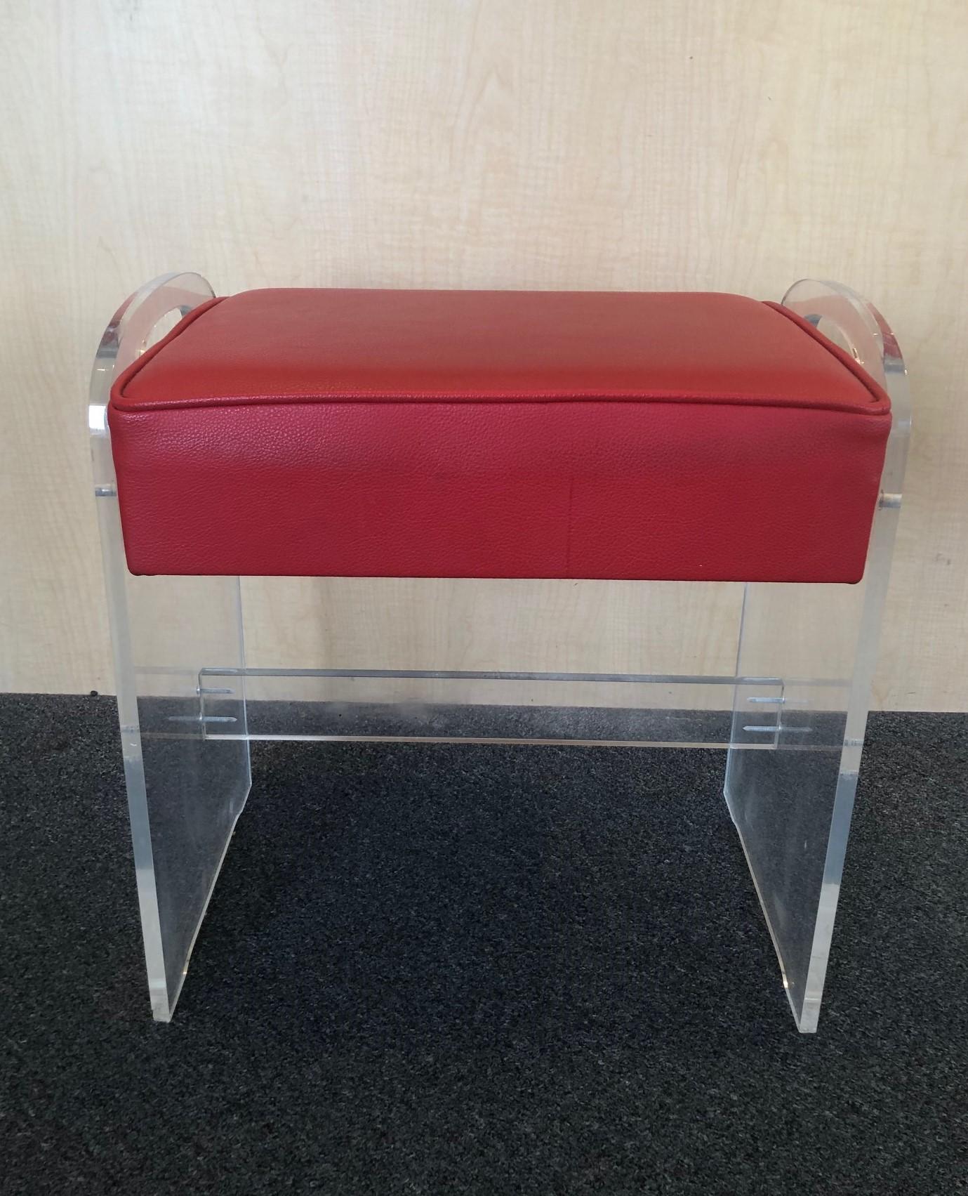 Postmodern Minimalist Lucite and red Naugahyde vanity stool with side handles, circa 1970s. The piece is in good vintage condition; very solid and stabile. There some scratches and crazing to the Lucite.