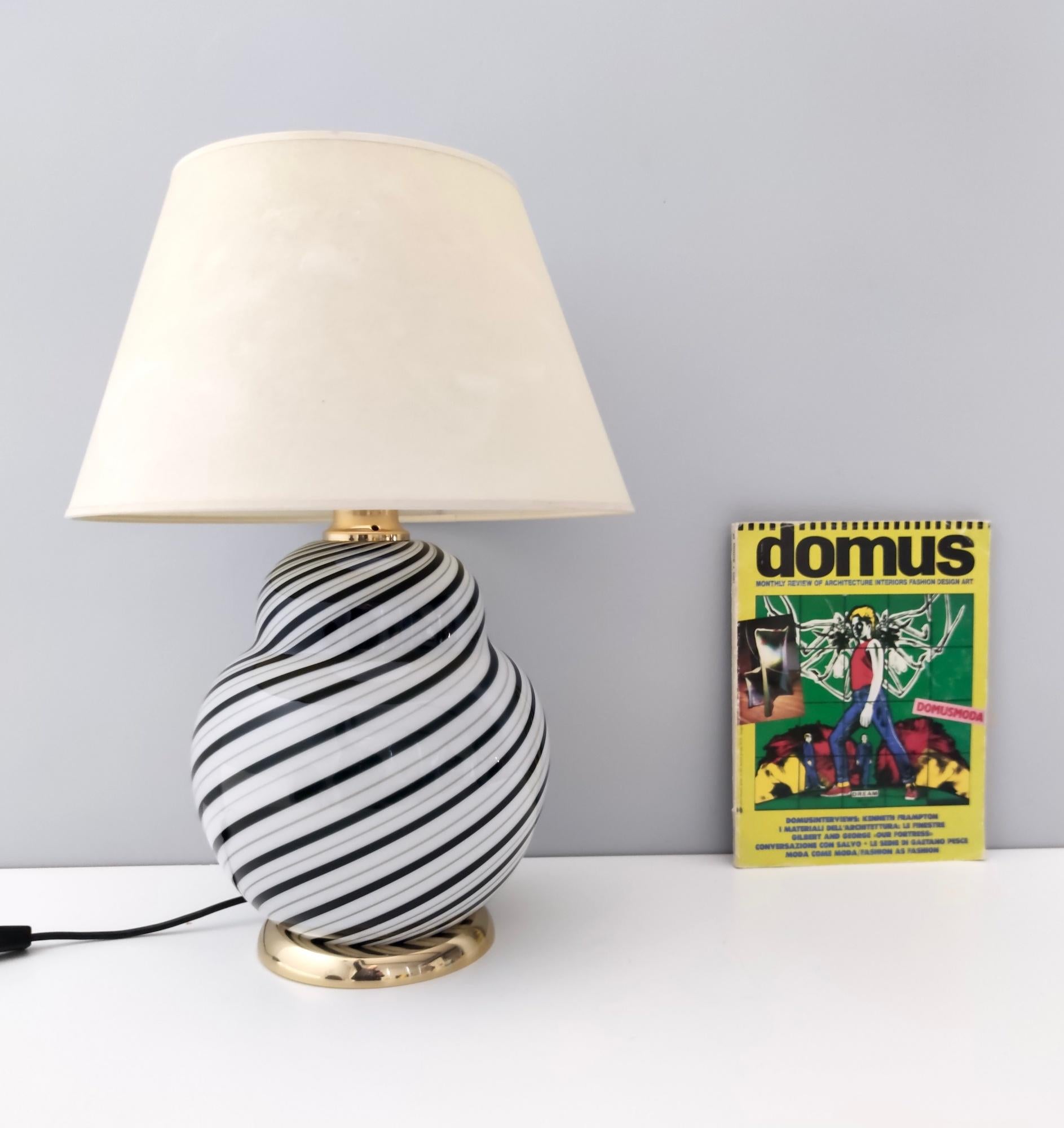 Fabriqué en Italie, années 1980. 
Elle est réalisée en verre de Murano noir et blanc, en laiton et en tissu.
Cette lampe à poser comporte deux lumières : elles peuvent être allumées séparément ou en même temps. 
Cette lampe peut présenter de légères