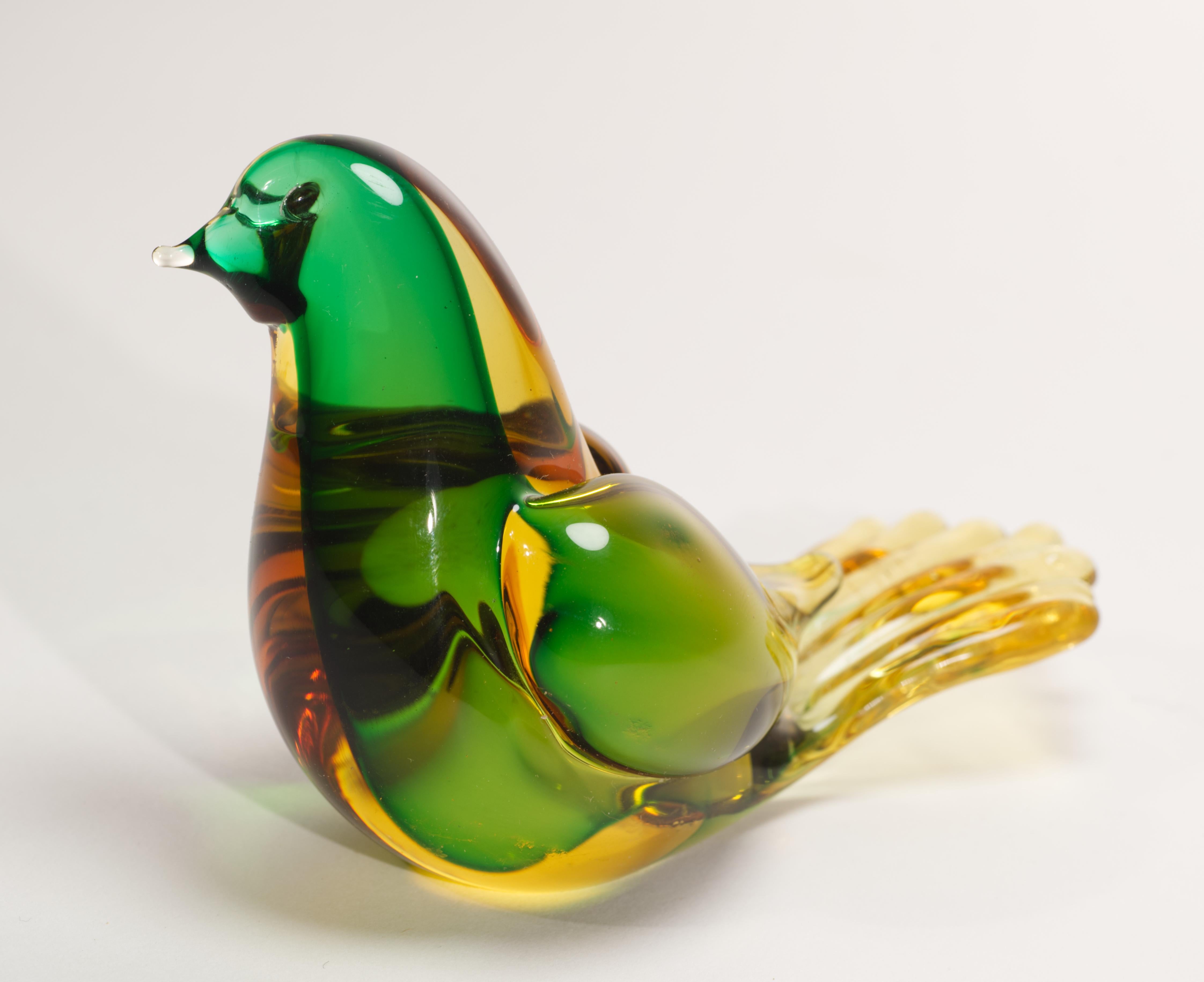  Playful bird figurine or paperweight is made in sommerso technique; green colored glass gather is cased over with amber-colored glass. Color contrast adds depth and movement to highly detailed shape of the piece. 

The figurine stands 3.18