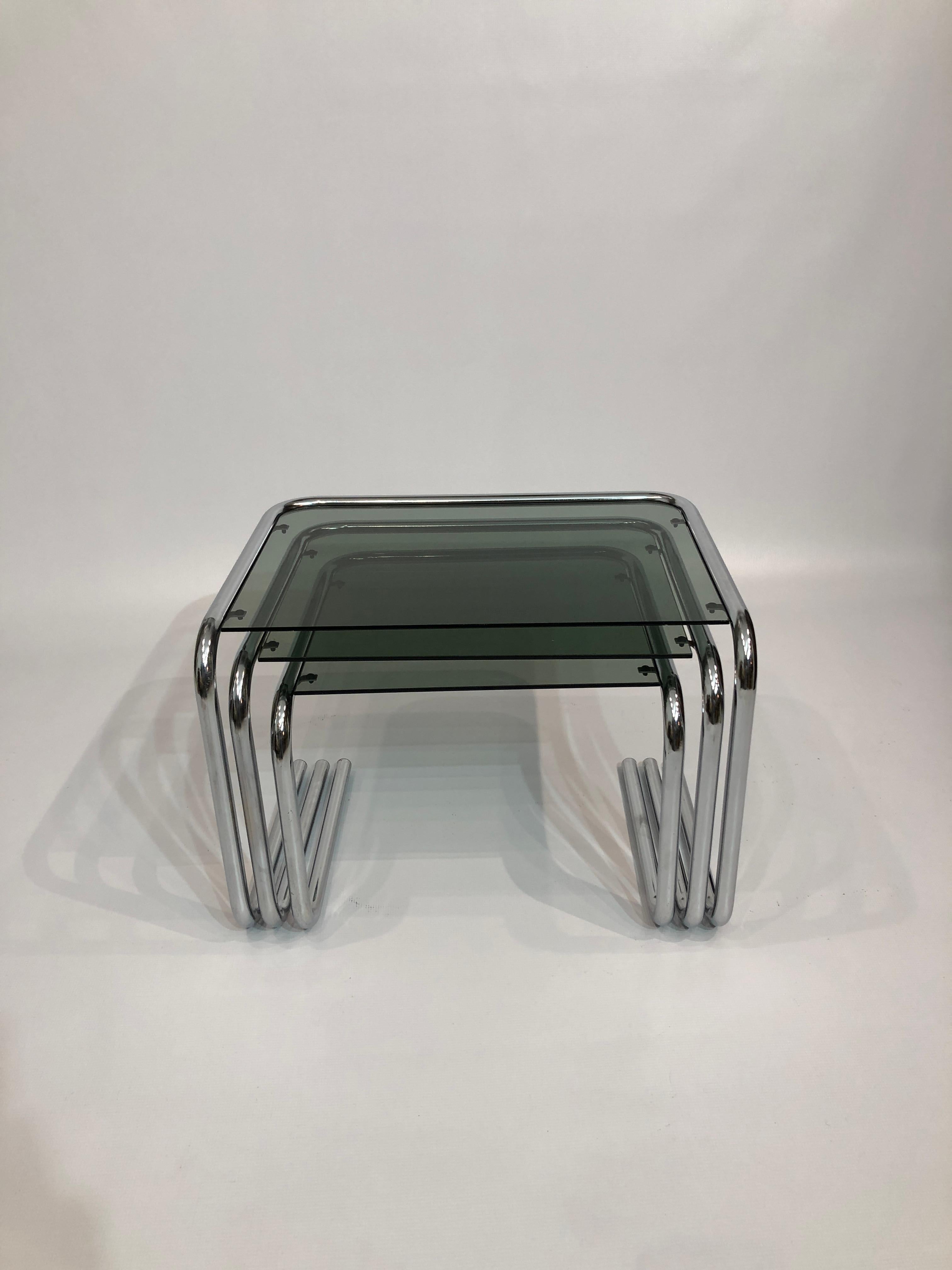 A nest of late-1970s Italian tables in chrome and smoked glass, featuring a smart cantilever design that oozes post-modern chic. 

The smoked green glass sits in a chrome frame, with tubular polygonal piping –– very much in the style of luxury