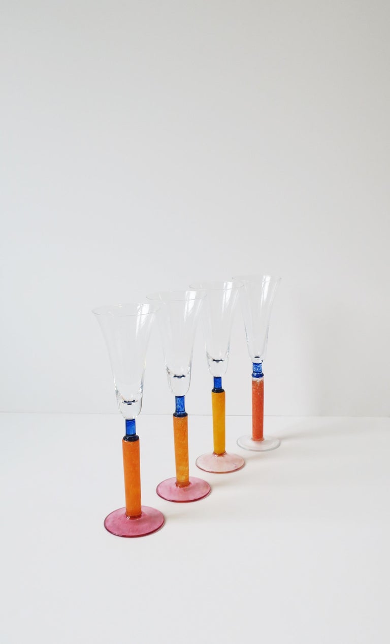 A beautiful set of four (4) Postmodern orange art glass Champagne flute glasses, circa 1990s, Europe. In the style of Kosta Boda, Sweden. Colors include: orange, pink, and blue. A beautiful set for home, summer, holiday entertaining, and for any