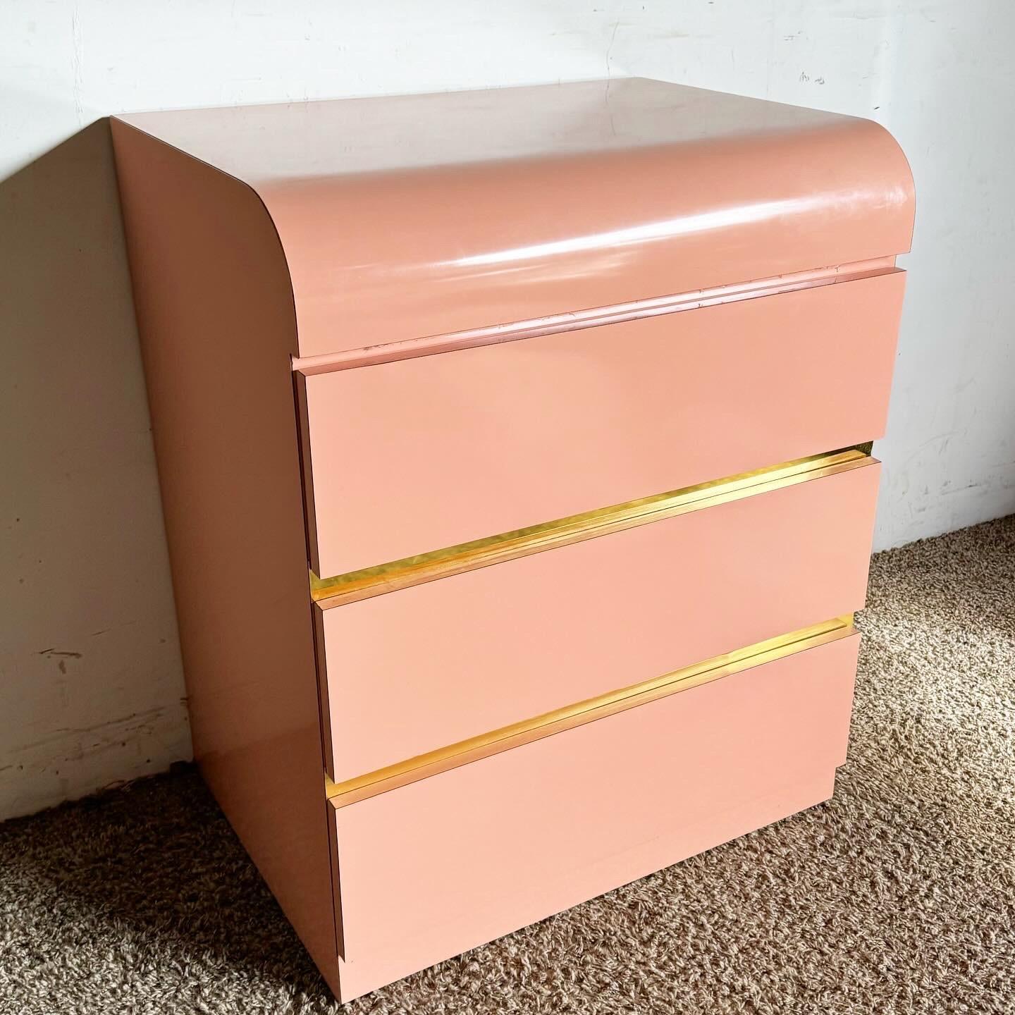 Add a vibrant and contemporary touch to your bedroom with the Postmodern Pink Lacquer Laminate and Gold Waterfall Nightstand/Commode. This piece features a sleek waterfall design in a striking pink hue, beautifully accented with luxurious gold. Its
