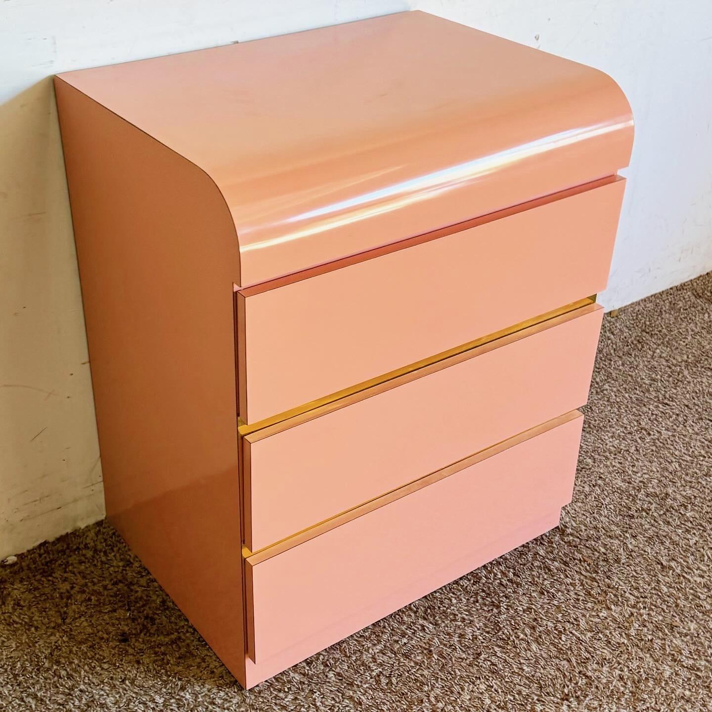 Discover the Pink Lacquer Laminate and Gold Waterfall Nightstand, a postmodern marvel featuring a vibrant pink finish and sleek gold accents. This piece combines bold aesthetics with functional elegance, perfect for contemporary interiors. Its