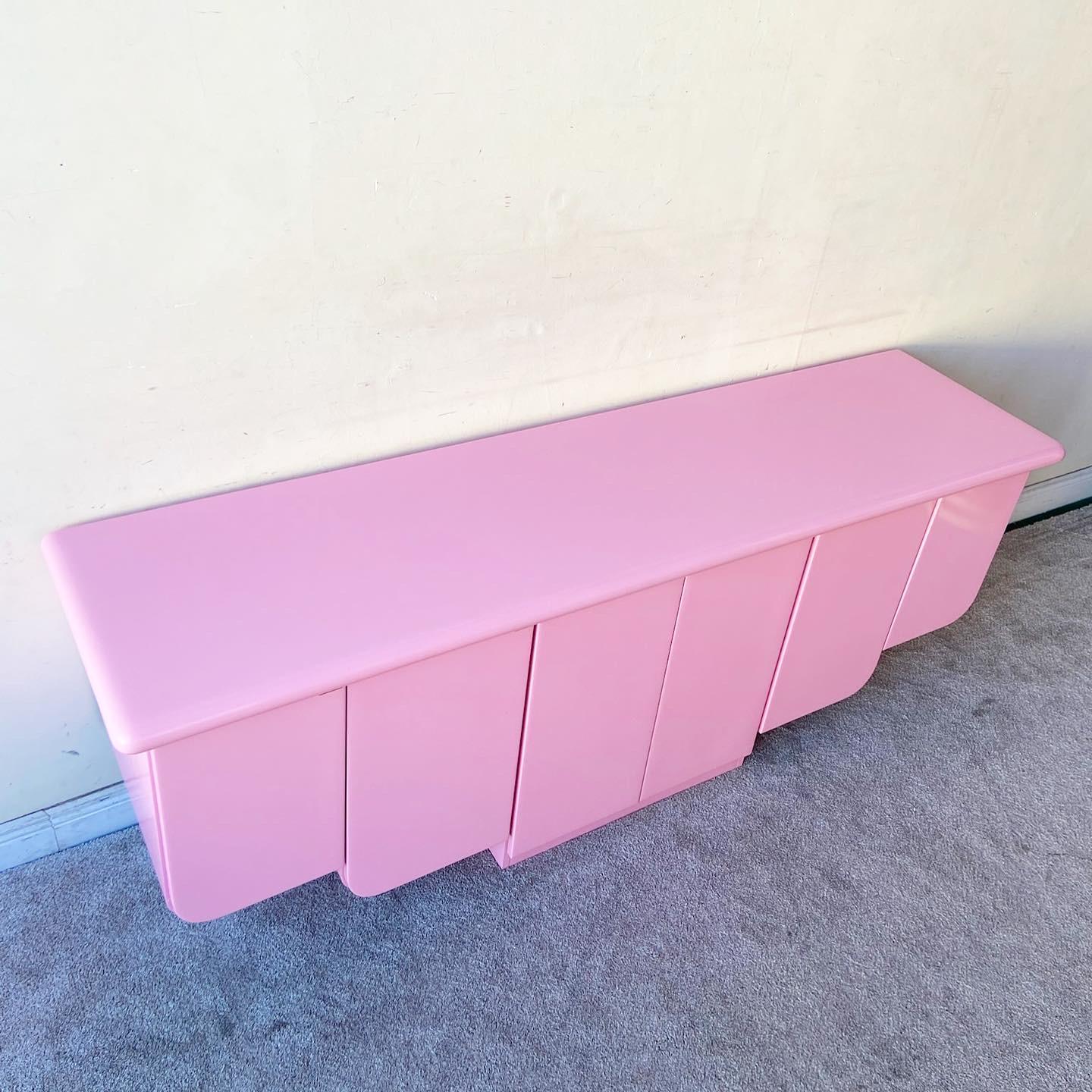 Phenomenal vintage postmodern credenza which has been refinished in a hot pink. Each door has a golden handle and opens to reveal shelved storage section ascending from the center.