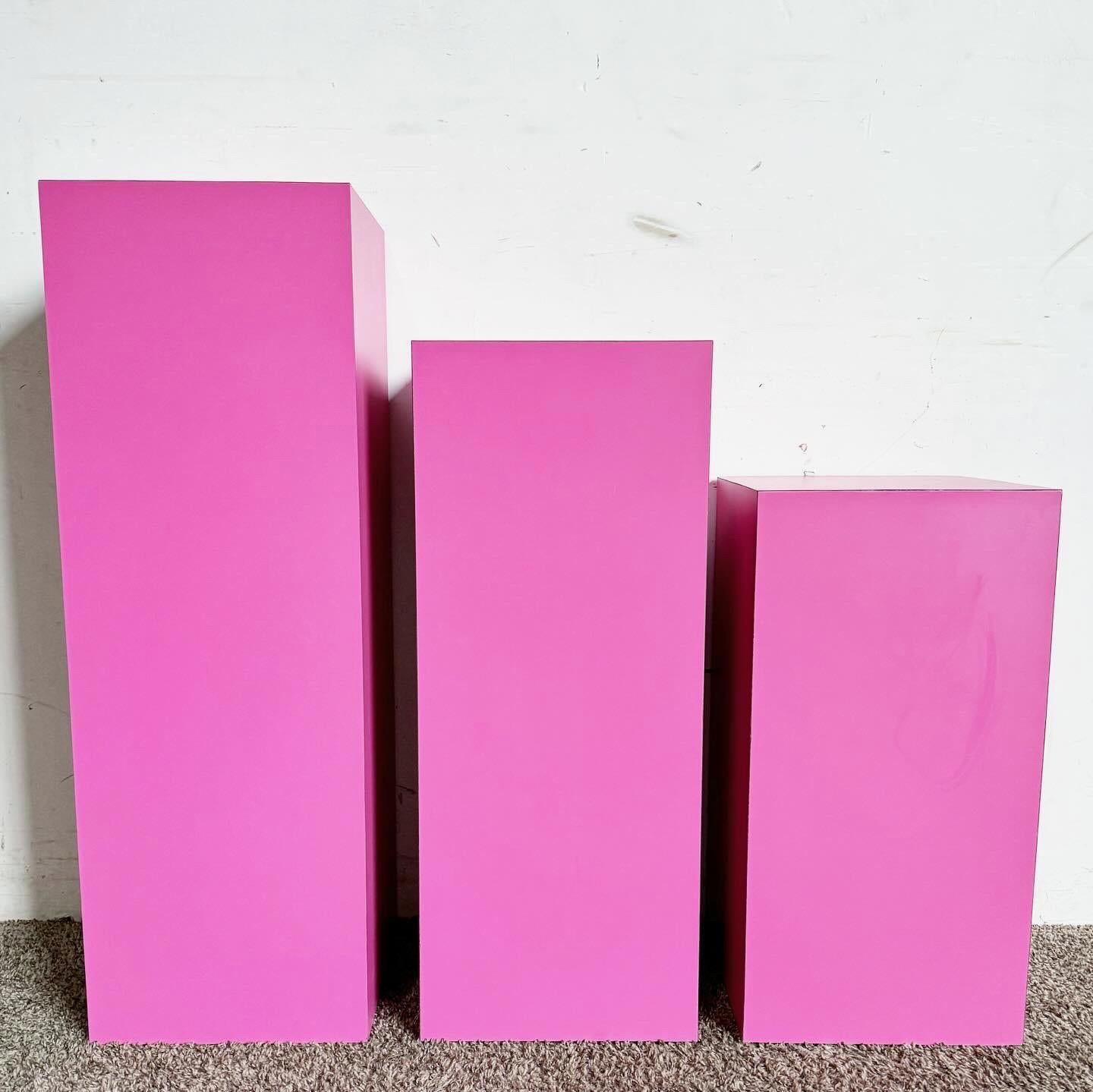 Invigorate your decor with the Postmodern Pink Matte Laminate Ascending Rectangular Prism Pedestal Tables, a set of three. These tables boast a lively pink matte finish, perfect for adding a dynamic pop of color. With heights of 36.25‚Äù, 30.25‚Äù,