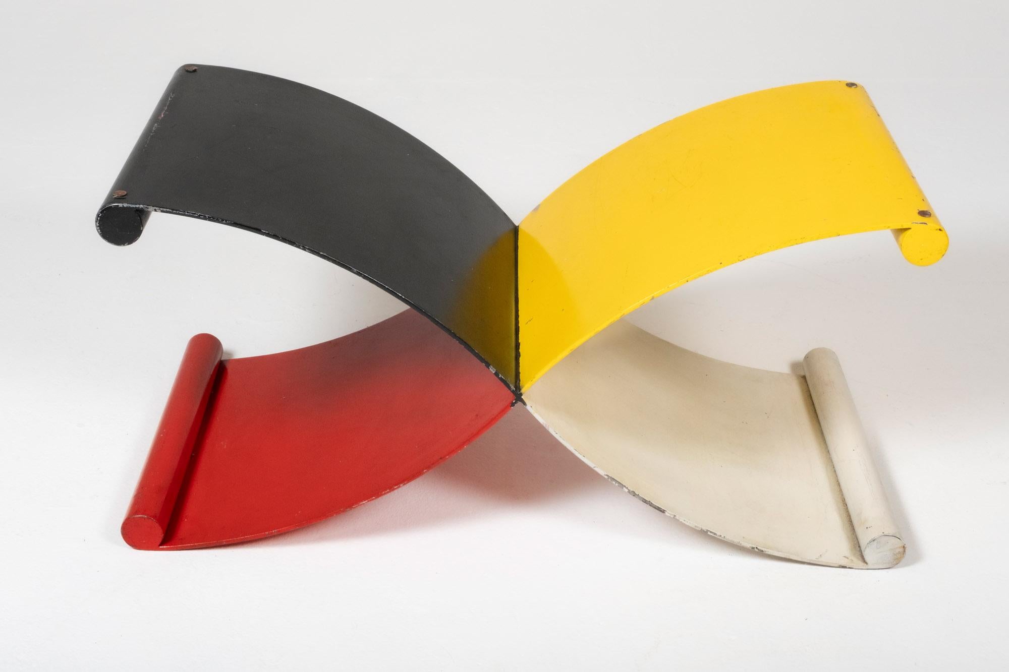 A dynamic postmodern coffee table base constructed from four intersecting curved iron forms, each painted in a bold primary tone—red, black, yellow, and white. The sculptural X-shaped design is visually engaging from every angle, offering both