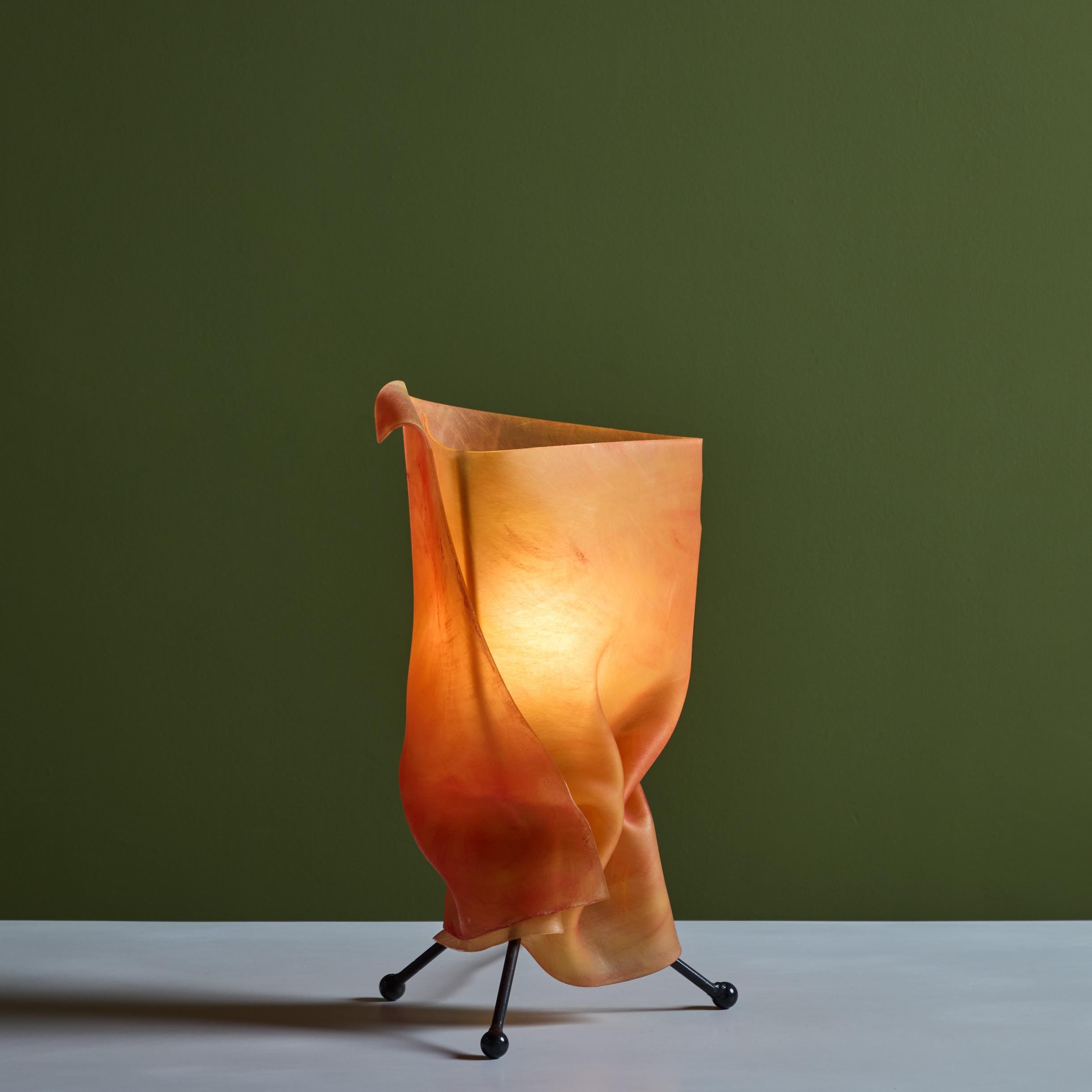 Postmodern table lamp with orange resin shade. The lamp is supported by three black enameled legs. The resin shade looks like a wrapped fabric and radiates a beautiful orange glow when on.

Dimensions
7.5