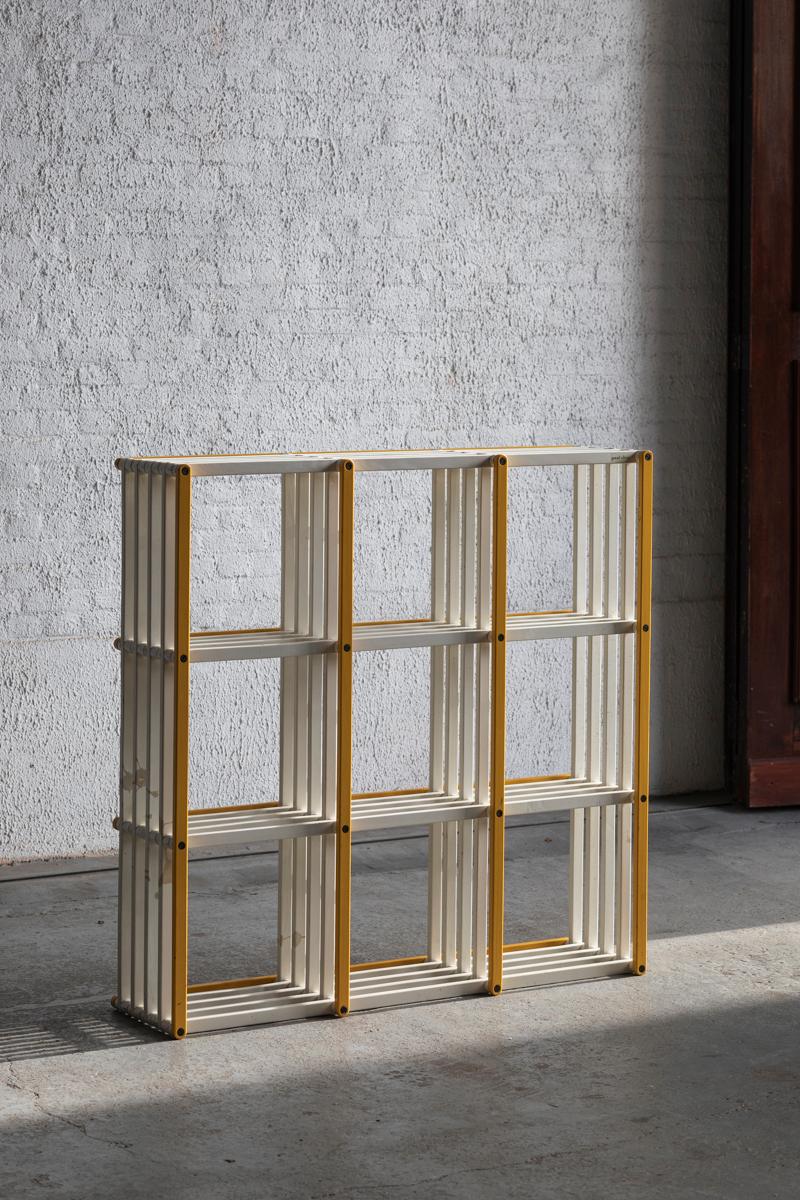 Postmodern shelving unit produced in Italy around 1980. The white and yellow lacquered wooden frame can be folded completely . In good condition with some scratches and greyish paint staining.

H: 109 cm
W: 107 cm 
D: 29 cm