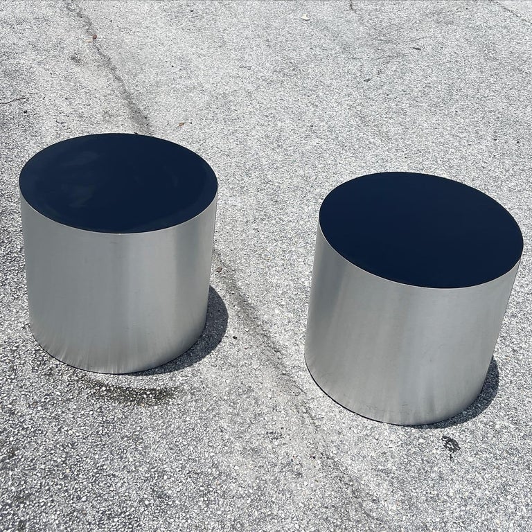 Incredible pair of cylindrical drum side tables. Each is paneles with a silver metal sheet and the top is a black laminate.
Each measure: 18”w, 18”d, 16”h.