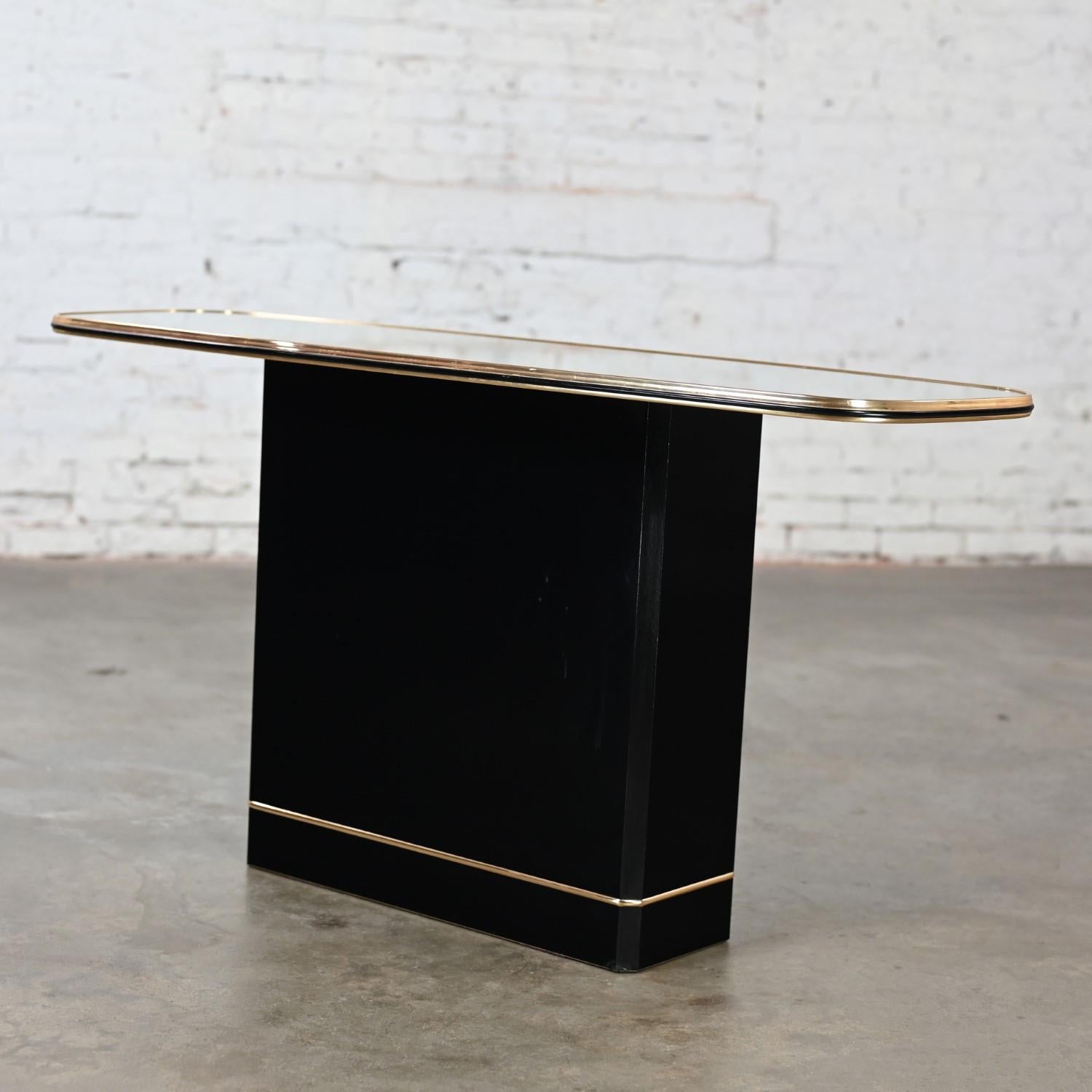 Magnificent vintage Postmodern sofa or console table comprised of a black lacquered pedestal base with beveled edges & gold base trim and a rounded rectangular shaped top with gold trim edges and mirror surface. Beautiful condition, keeping in mind