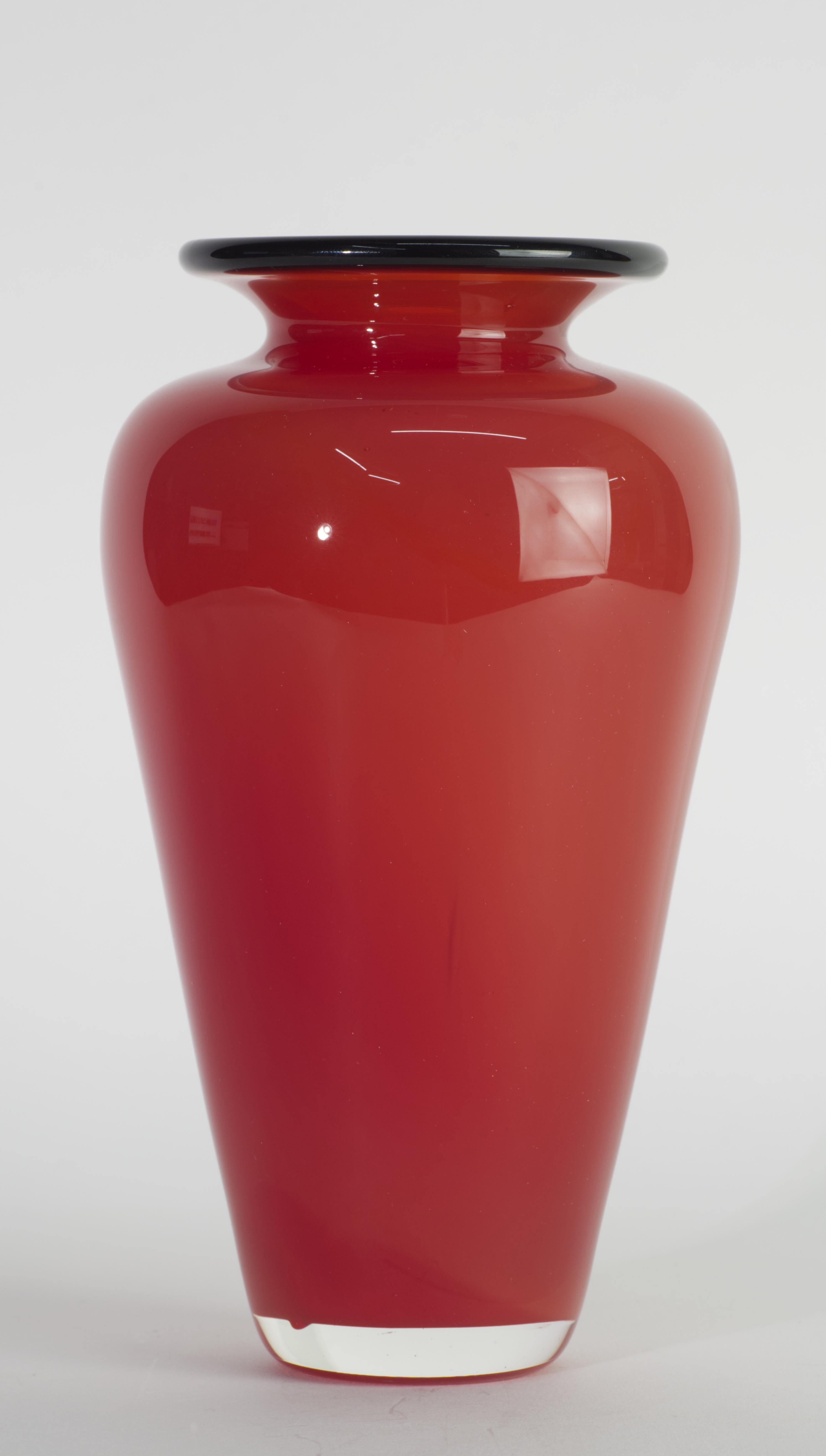 El jarrón escultórico de vidrio artístico se creó con una forma alargada y gráfica, con un cuerpo rojo semitransparente recubierto de vidrio transparente en técnica de sommerso; el borde del jarrón está decorado con vidrio negro fundido, que crea un