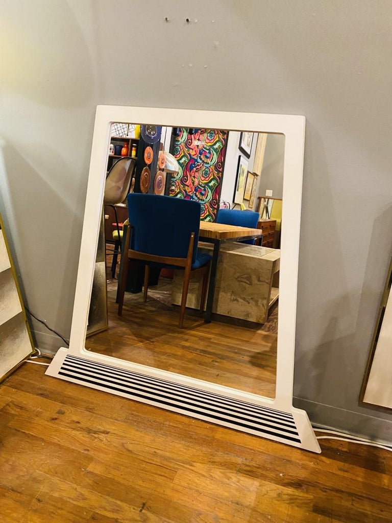 This very unique wall mirror brings postmodern and space age lines together to create a piece that’s striking yet timeless. The mirror has a white lacquer finish that contrasts with a graduation of black lines design at the base that bring a