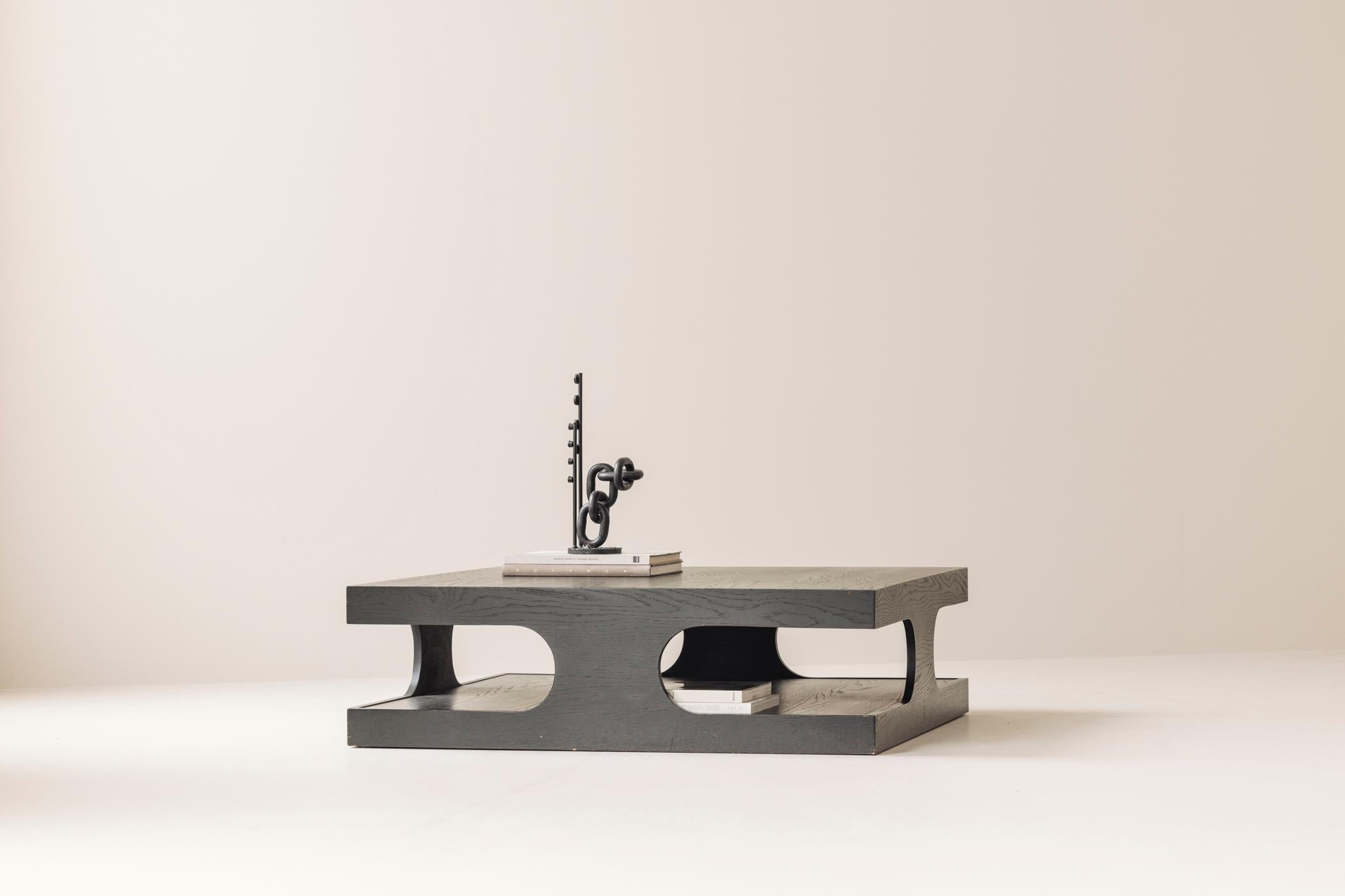 Bold in presence yet refined in detail, this striking square coffee table from the 1980s is a standout piece of postmodern design. Crafted from dark-stained oak, the table features a dynamic two-tier silhouette, with cut-out side panels that create