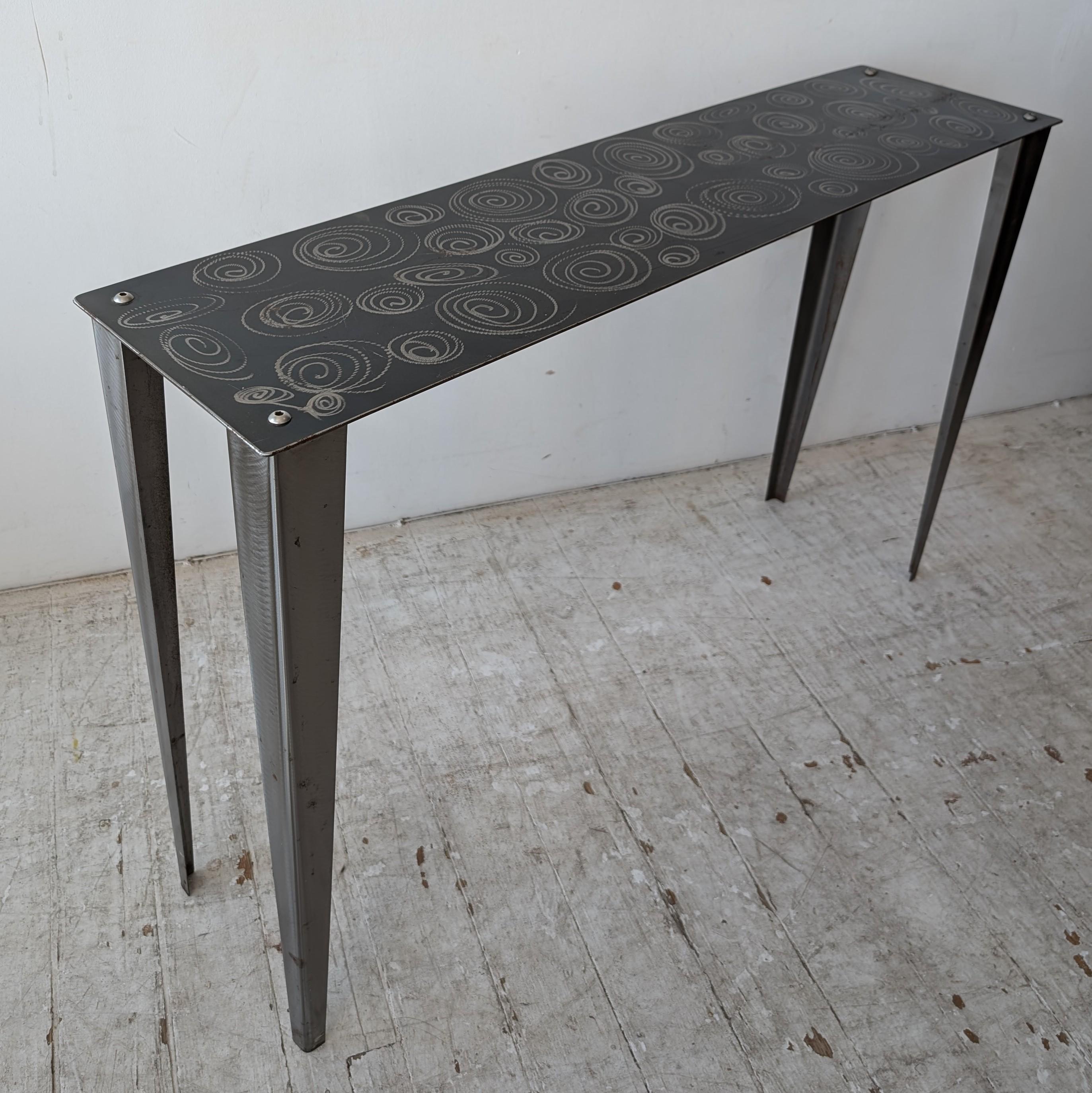 Stylish skinny postmodern steel console table with spiral squiggle design. USA 1980s/ 90s. Some wear to surface on right hand side (see video)

Dimensions: width 120.5cm, depth 30.5cm, height 77cm