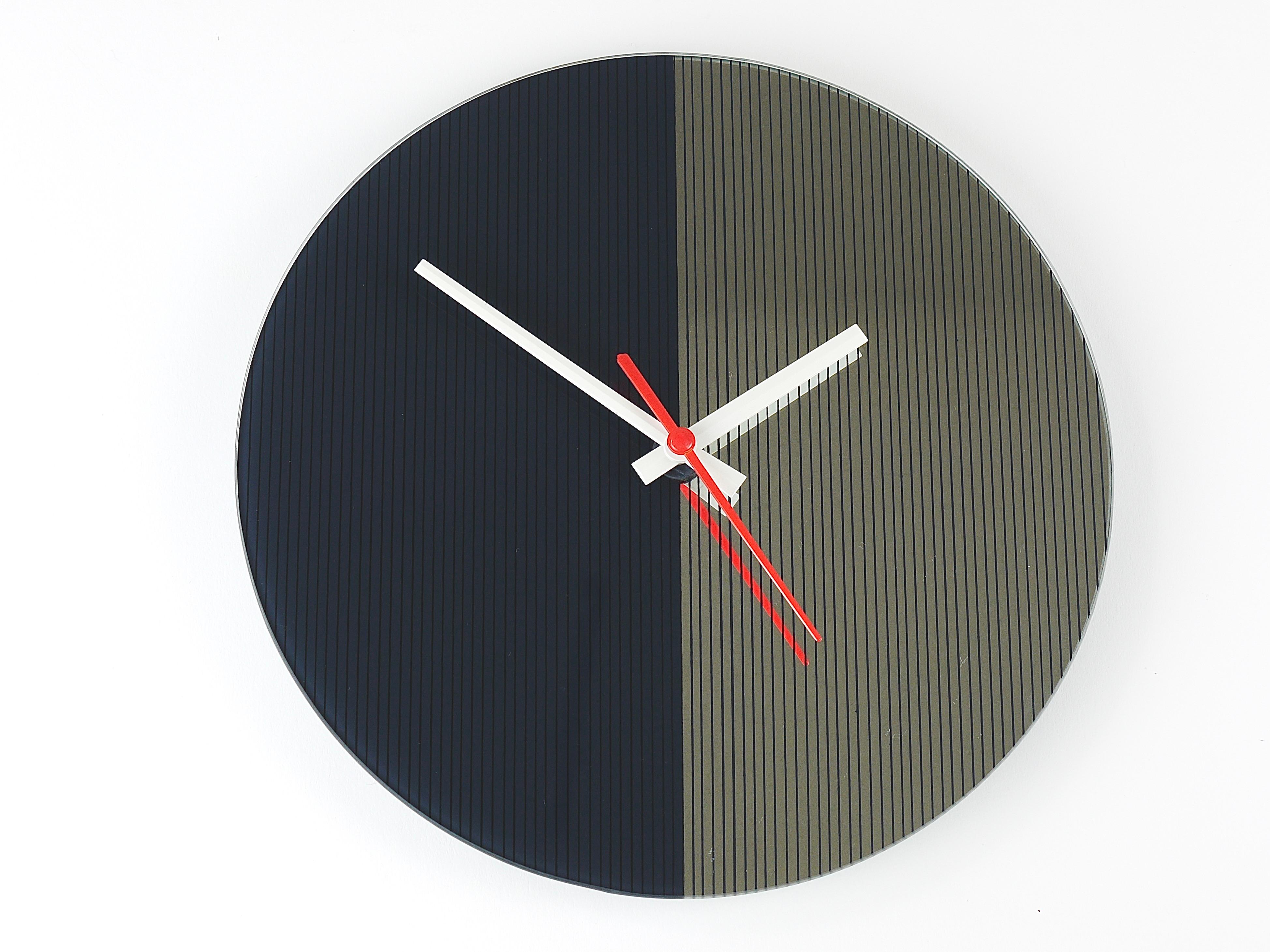 A beautiful post-modern Memphis-style vintage wall clock from the 1980s, made in England. It features a two-tone mirrored glass face with fine black pinstripes — the left side in a darker shade and the right side in reflective mirror glass. The