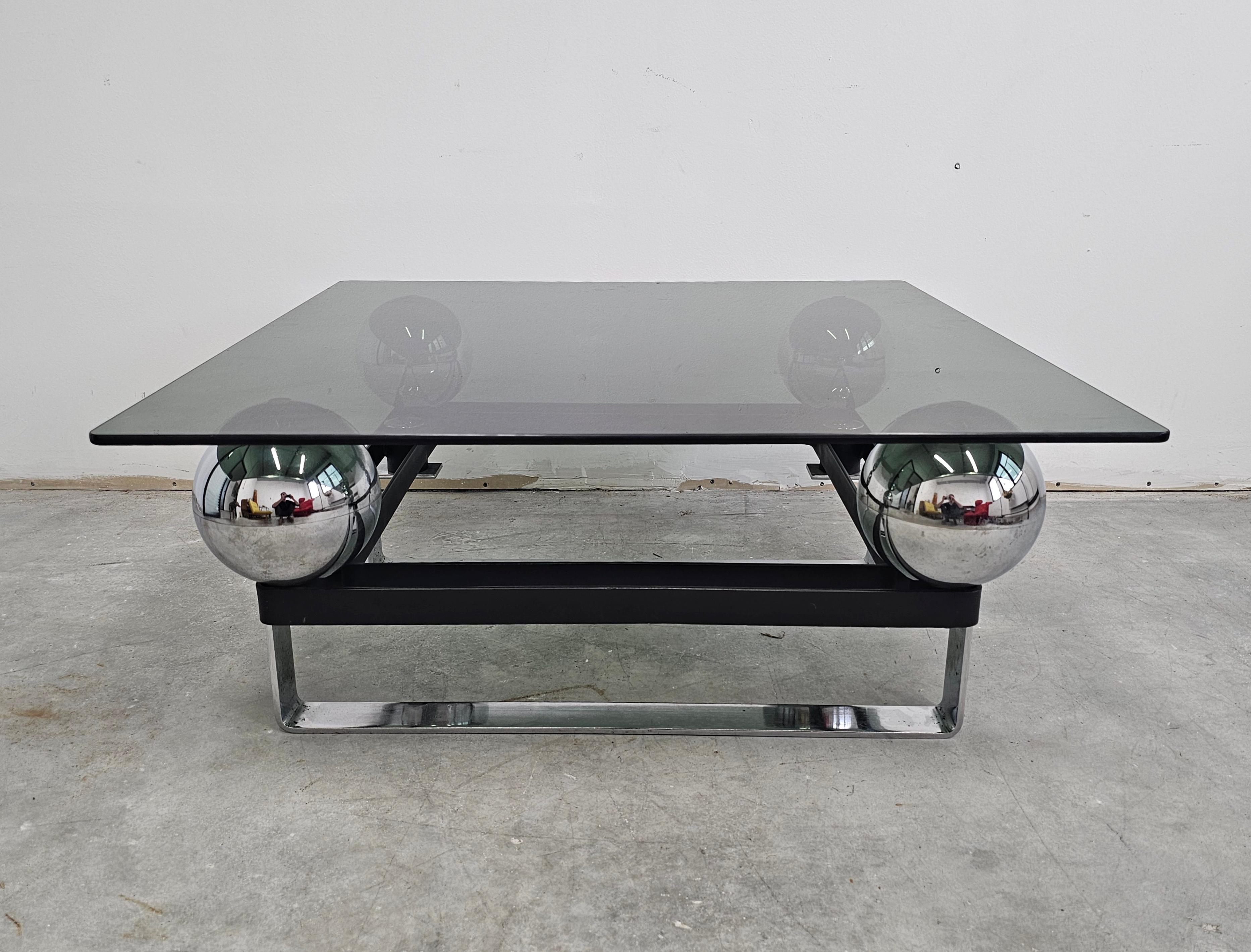 In this listing you will find a spectacular postmodern coffee or cocktail table done in chrome plated steel, with a tinted glass top. The original smoked glass top floats on four large chromed orbs. Evocative of the designs of Maria Pergay. Made in
