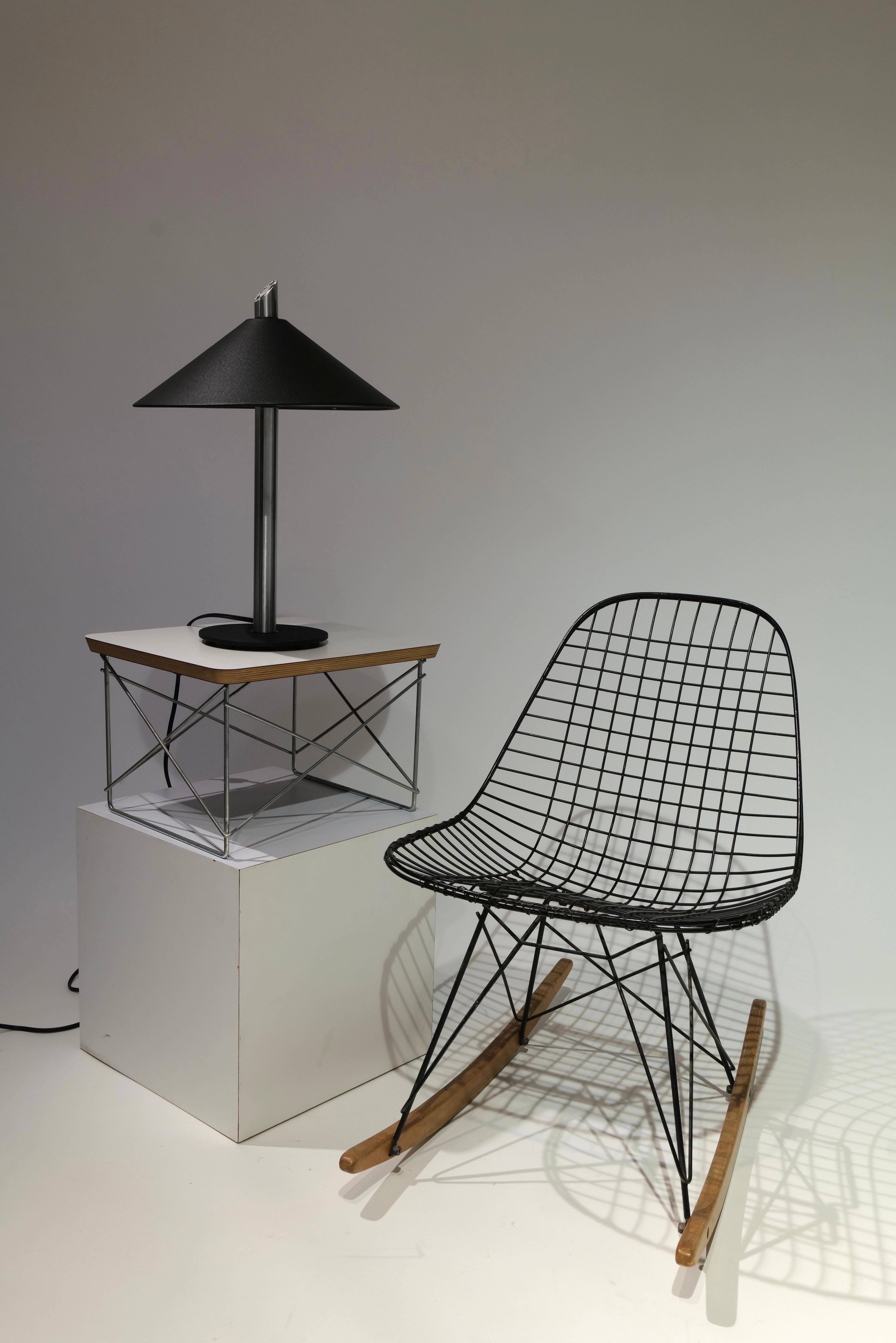 Esta lámpara de sobremesa, un sorprendente ejemplo de diseño posmoderno, presenta una silueta audaz y geométrica que equilibra los materiales industriales con la elegancia escultural. La pantalla cónica negra ofrece un contraste espectacular con el