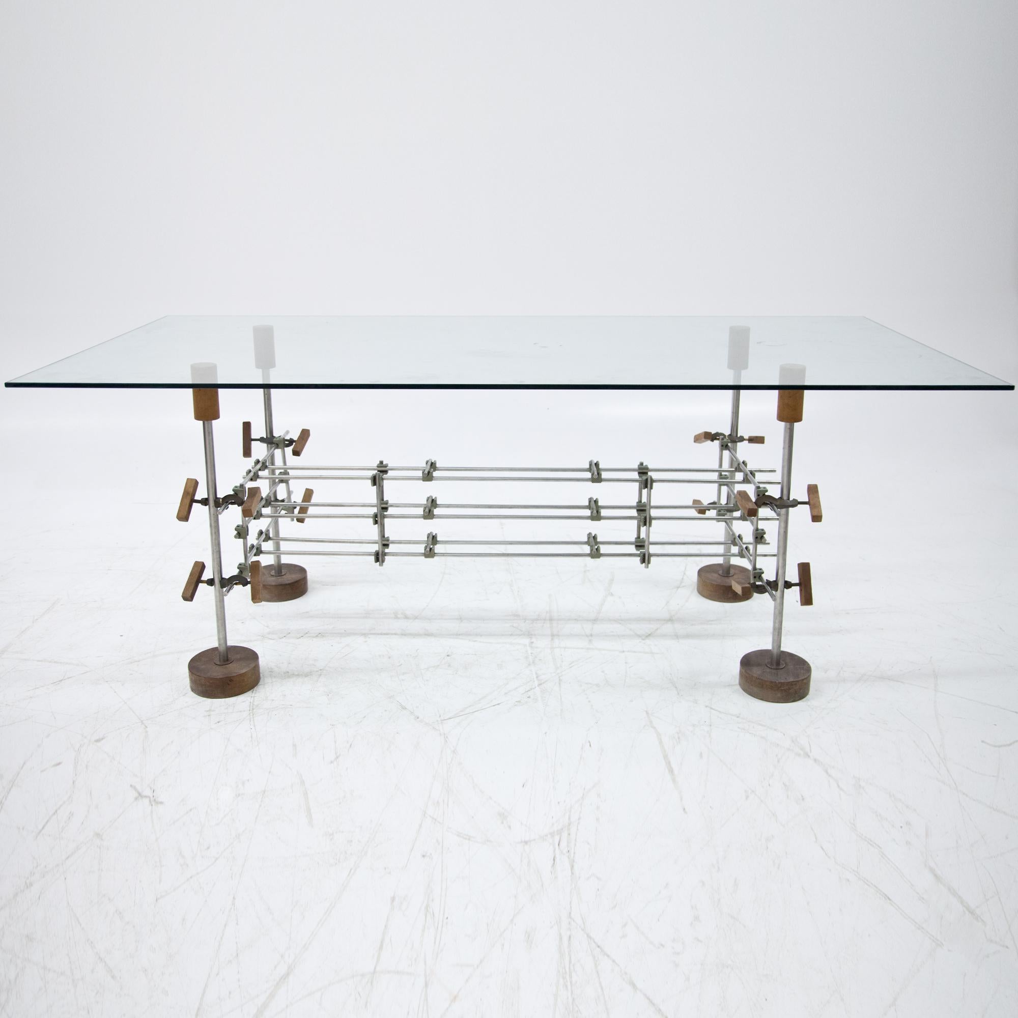 Table on round wooden discs, with unusual steel frame made of individual struts and fixings in the form of clamps. Glass table top.