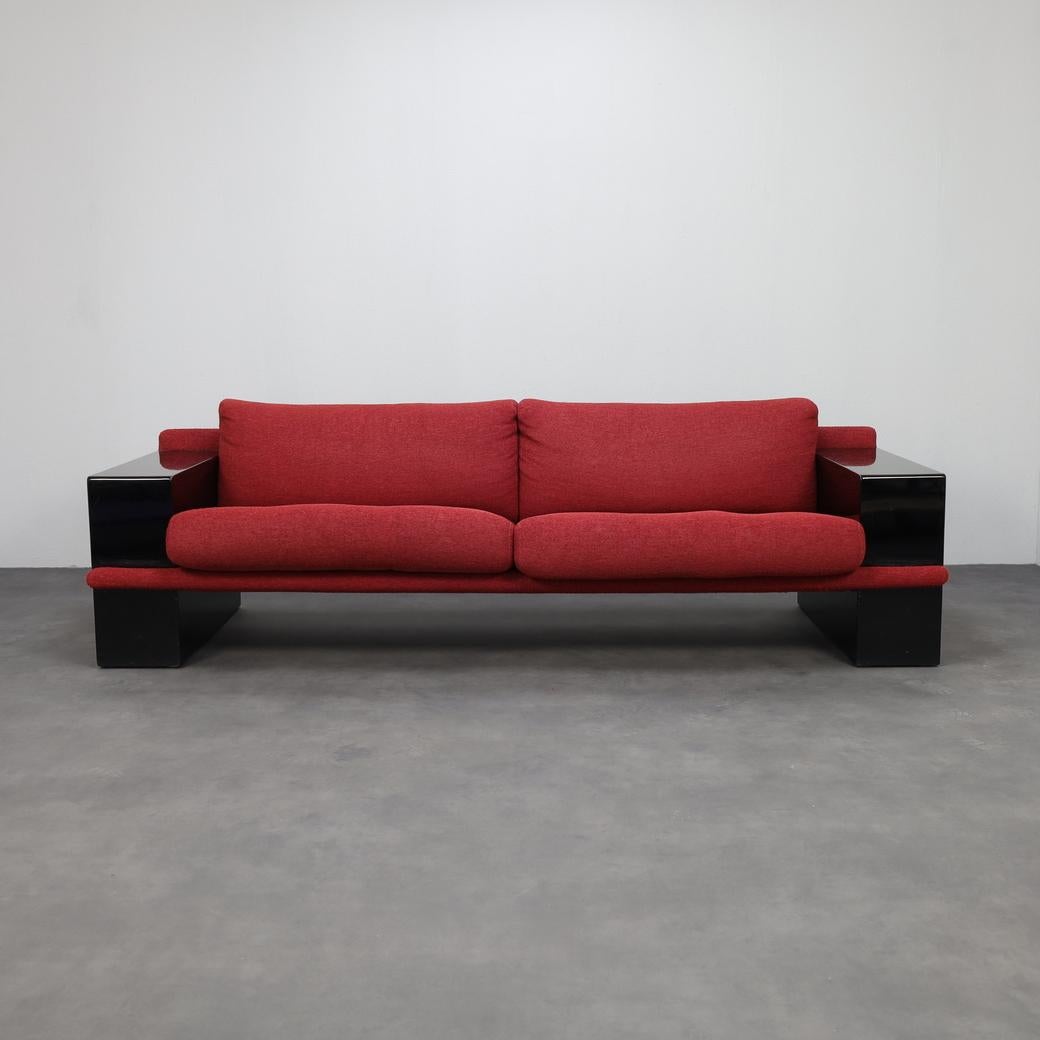 Striking postmodern three-seater sofa from Italy, dating to the 1980s. With its bold black lacquered frame and deep red fabric cushions, the design balances sculptural presence with inviting comfort. A strong geometric silhouette and contrasting