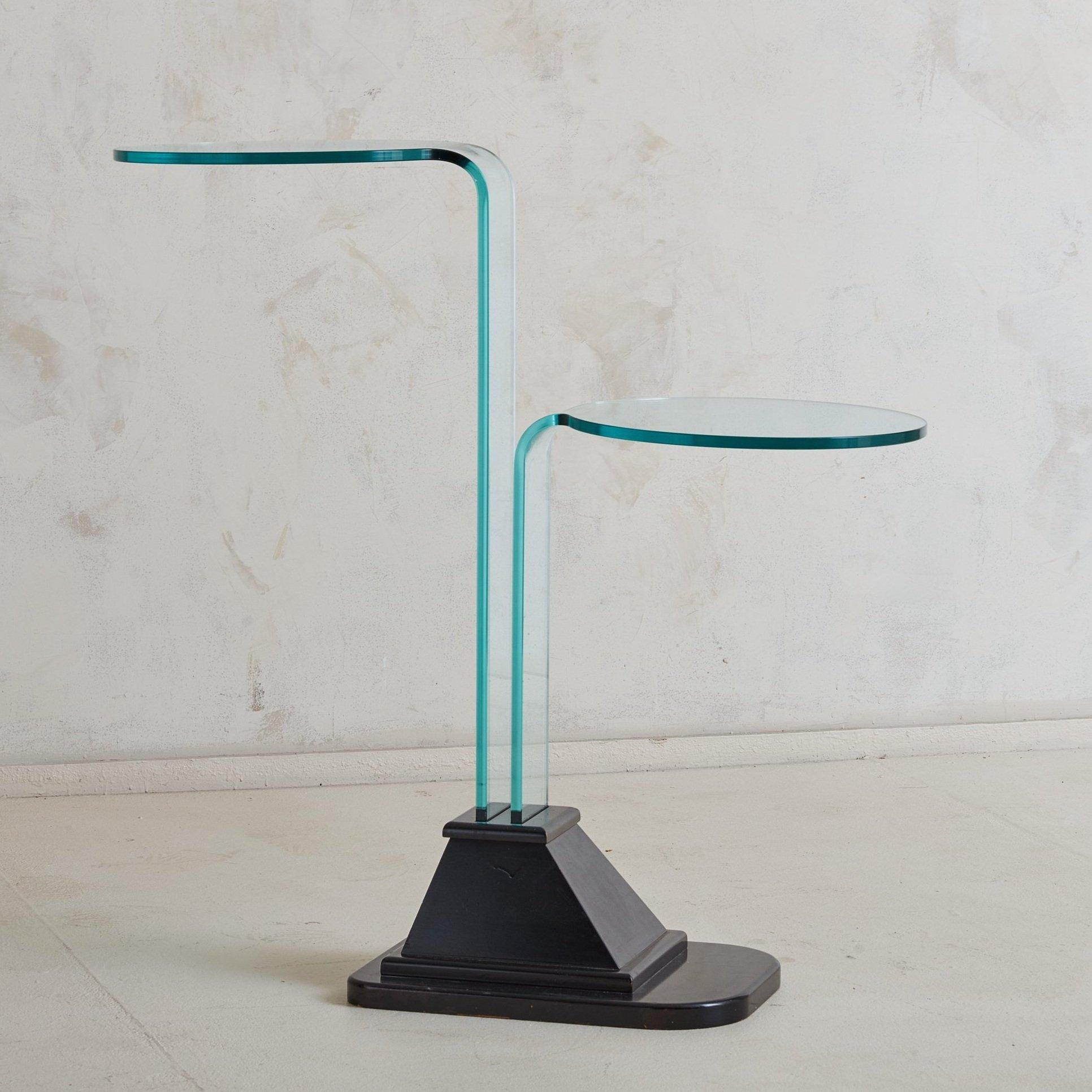 An Italian Postmodern wood and glass two tier side table from the 1980s. This table is composed of a geometric wood base and two vertical glass sheets that curve horizontally, creating surface space. The glass has a turquoise tinge, contrasting