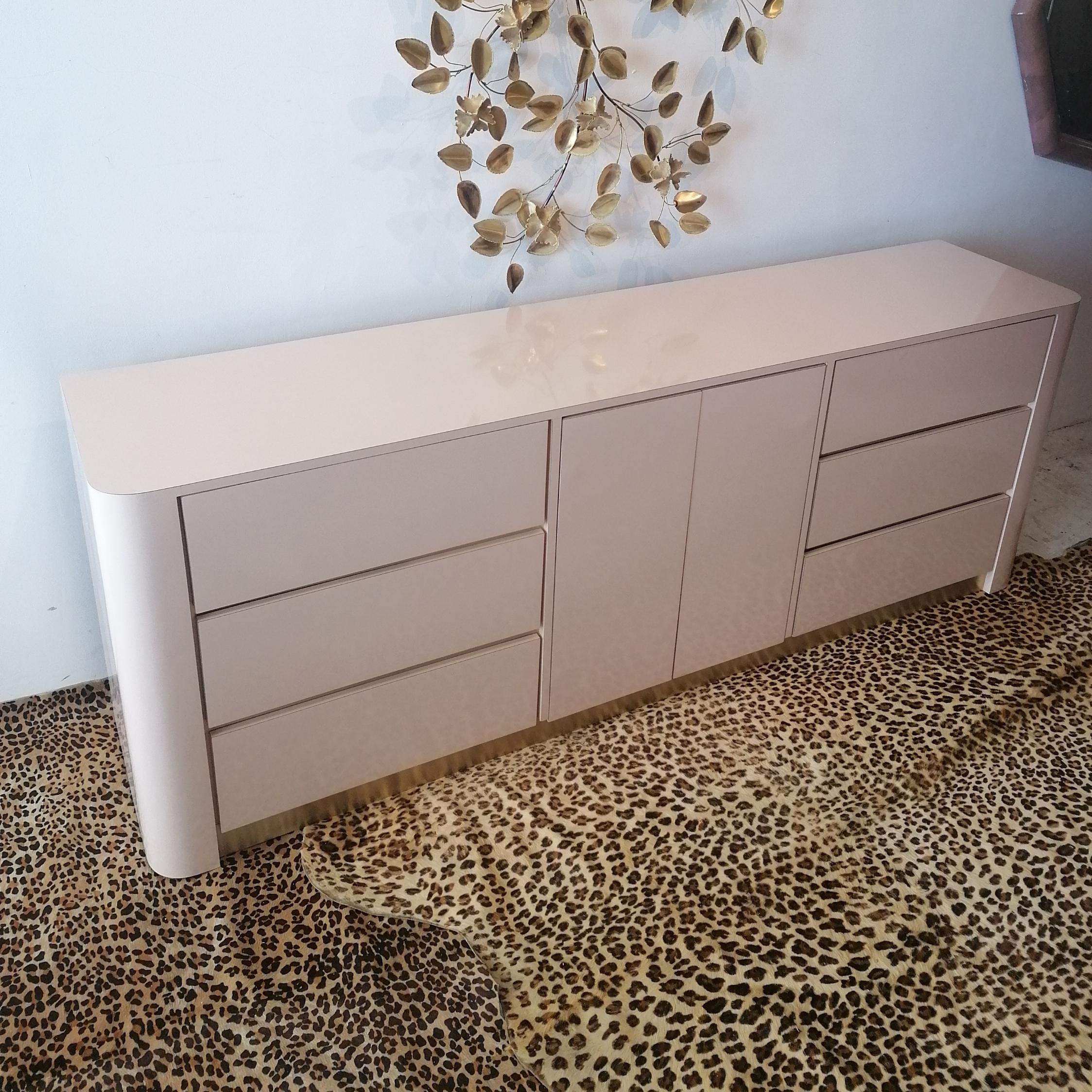 Long postmodern 1980s American pale blush pink laminate sideboard / dresser with drawers. Gold metal trim between drawers and along base.
Three drawers left and right. Central doors open to reveal three inner drawers.
In great condition- just a