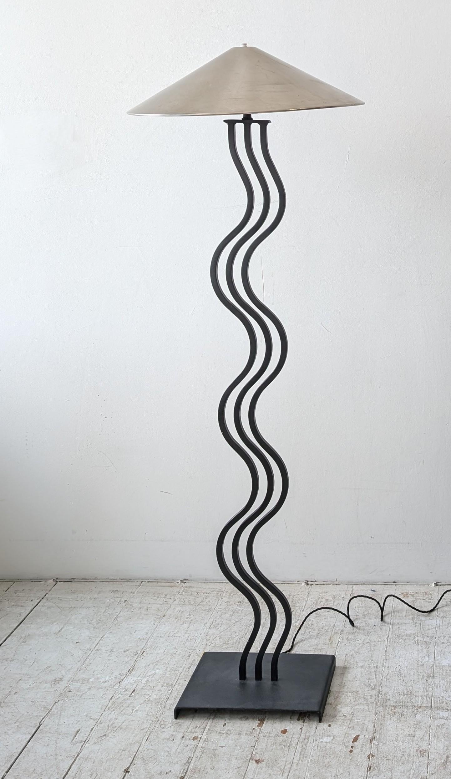 Postmodern black metal wiggle floor lamp, with brushed steel shade. USA 1980s.
Newly rewired with braided cord 

Dimensions: height to top of shade 138cm, diameter of shade 46cm, width of base 30cm, depth of base 20.5cm