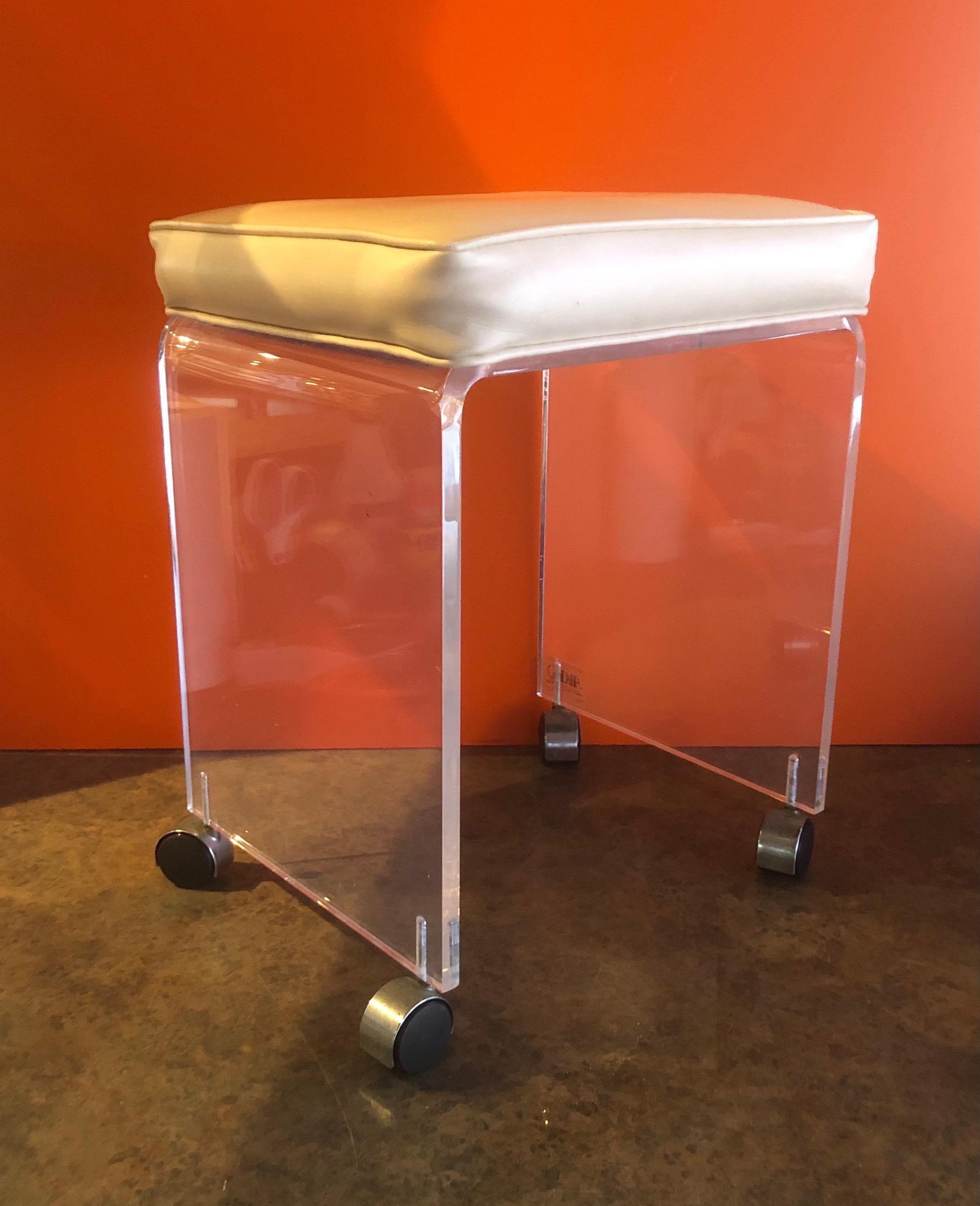 Postmodern waterfall Lucite vanity stool or bench by Akko, circa 1970s. The bench has a cream colored Naugahyde seat and is in good vintage condition; very solid and stabile. There some scratches, crazing and fogging to the Lucite. #1298.
