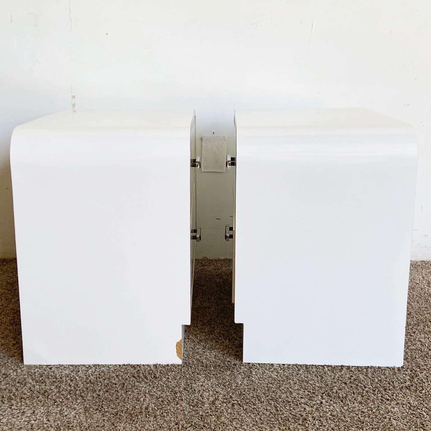 Exceptional pair of vintage postmodern waterfall nightstands. Each feature a white lacquer laminate with gold accents and lucite drawer pulls.