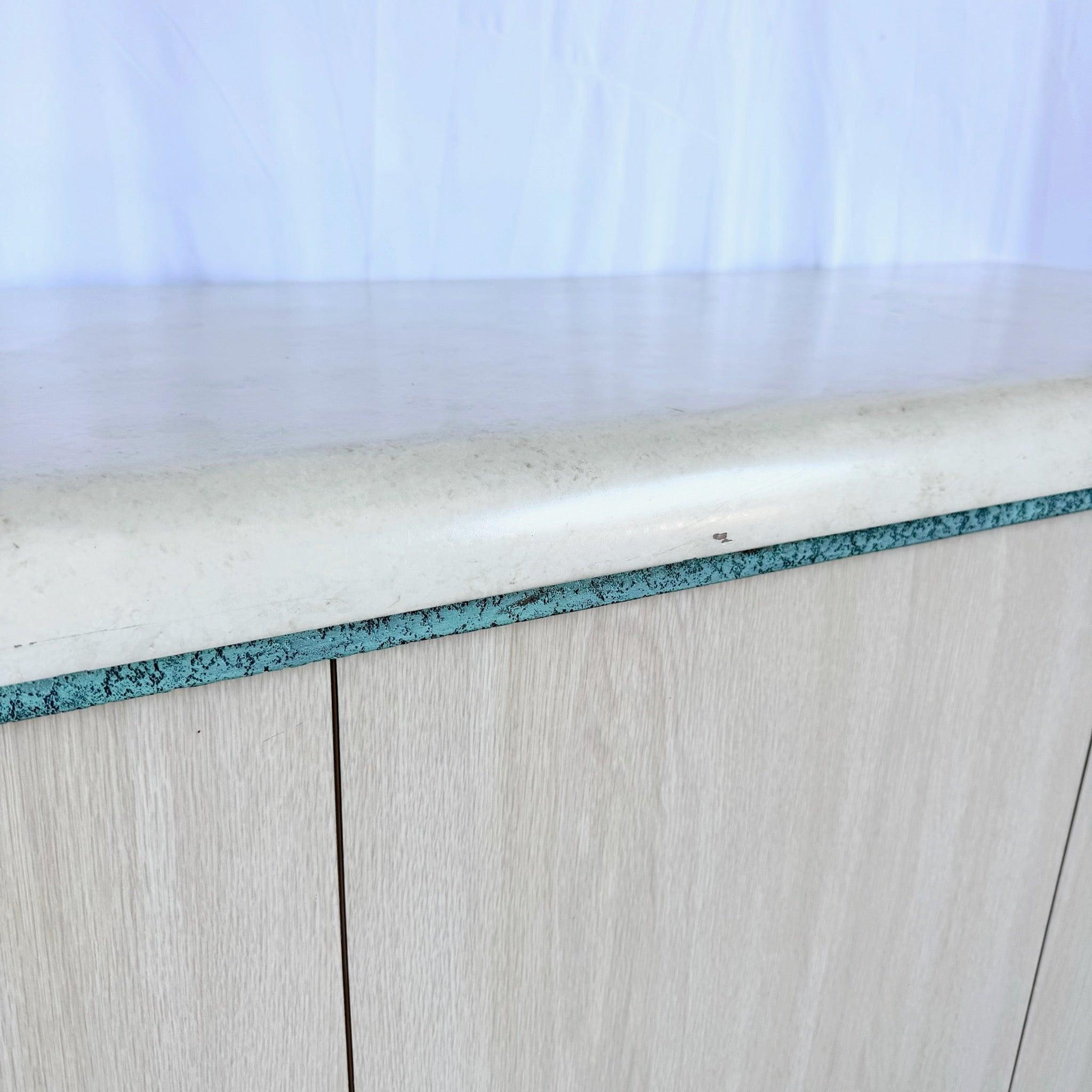 Haz una declaración audaz con esta Credenza Postmoderna Acentuada en Turquesa: laminado de grano de madera, metal turquesa tribal y herrajes cromados en una sola pieza.
 

 Algunos desconchones alrededor de la base y los bordes, como puede verse en