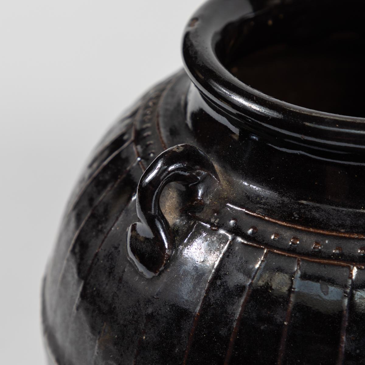 This ming style pot dates from the mid 19th century. It is finished in a black glaze and features a number of small handles near the rim. It measures 9 inches in height and 9.5 inches in diameter. 