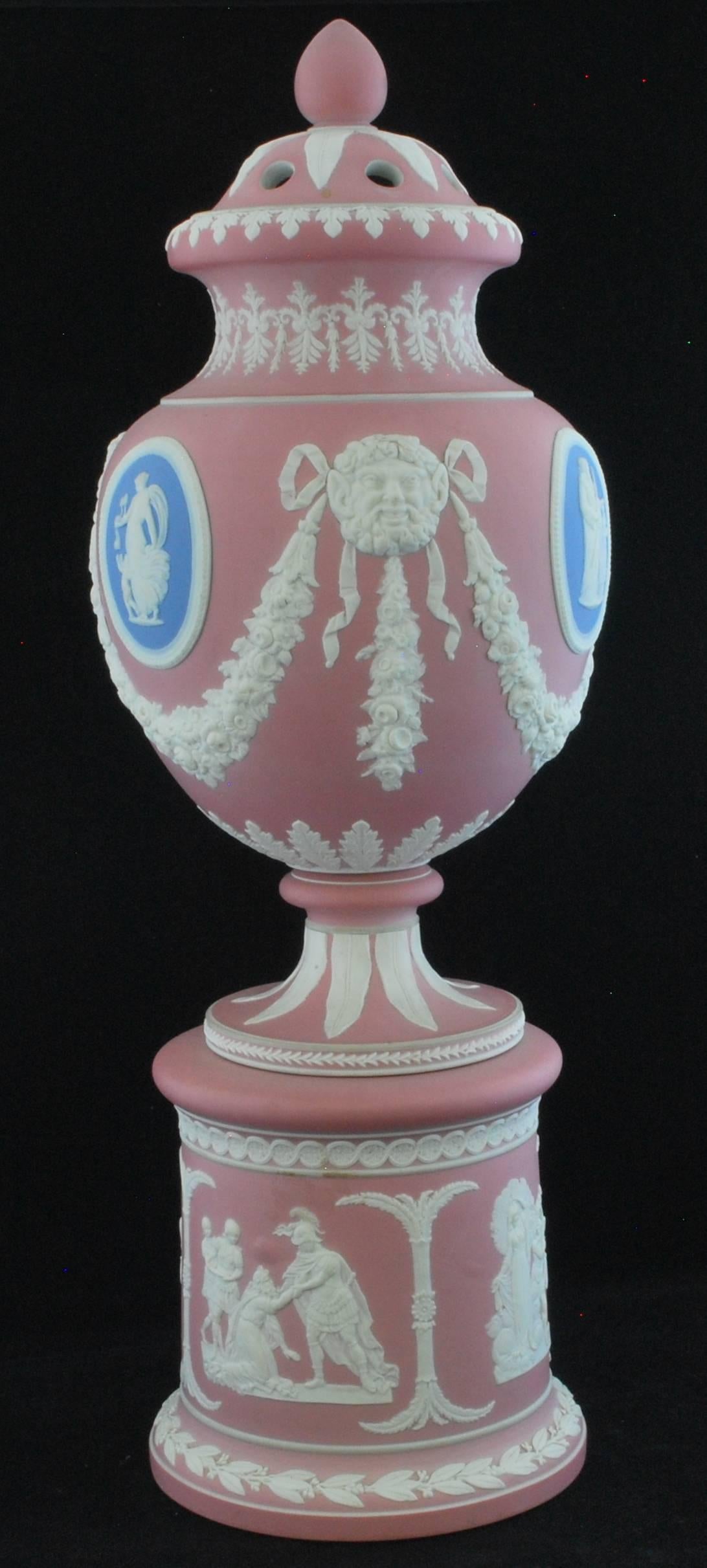 A tall vase on a drum base, in Dudson's distinctive pink jasperware, set with blue and white reliefs.

Dudson was an imitator of Wedgwood, and often left their wares unmarked with the intention that they would be mistaken for it. The quality is