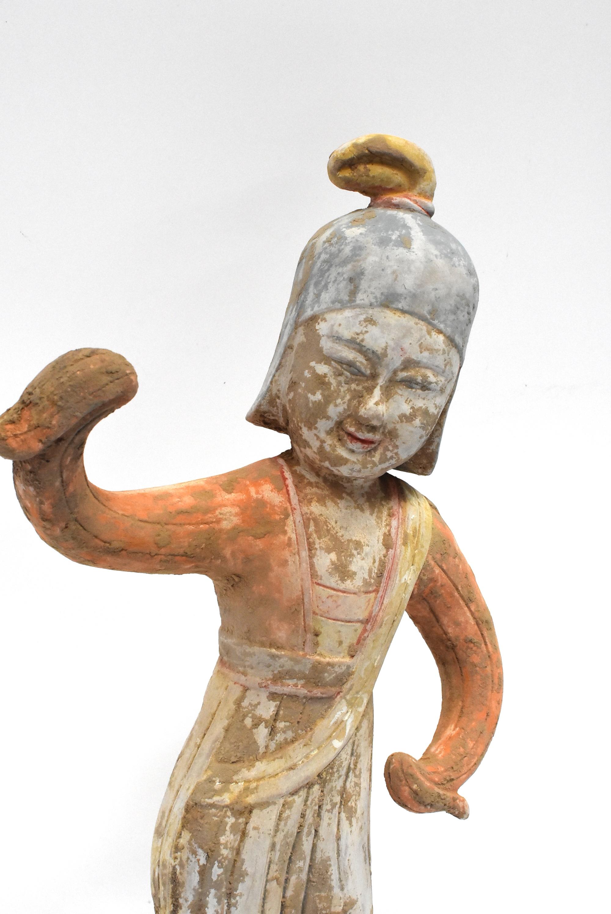 A beautiful pottery figure, Han style, in orange and pastel colors. What's special about this piece is the figure's facial expression. She is joyful. A pale blue military style helmet indicates her dance is of a sort that is a tribute to victory.