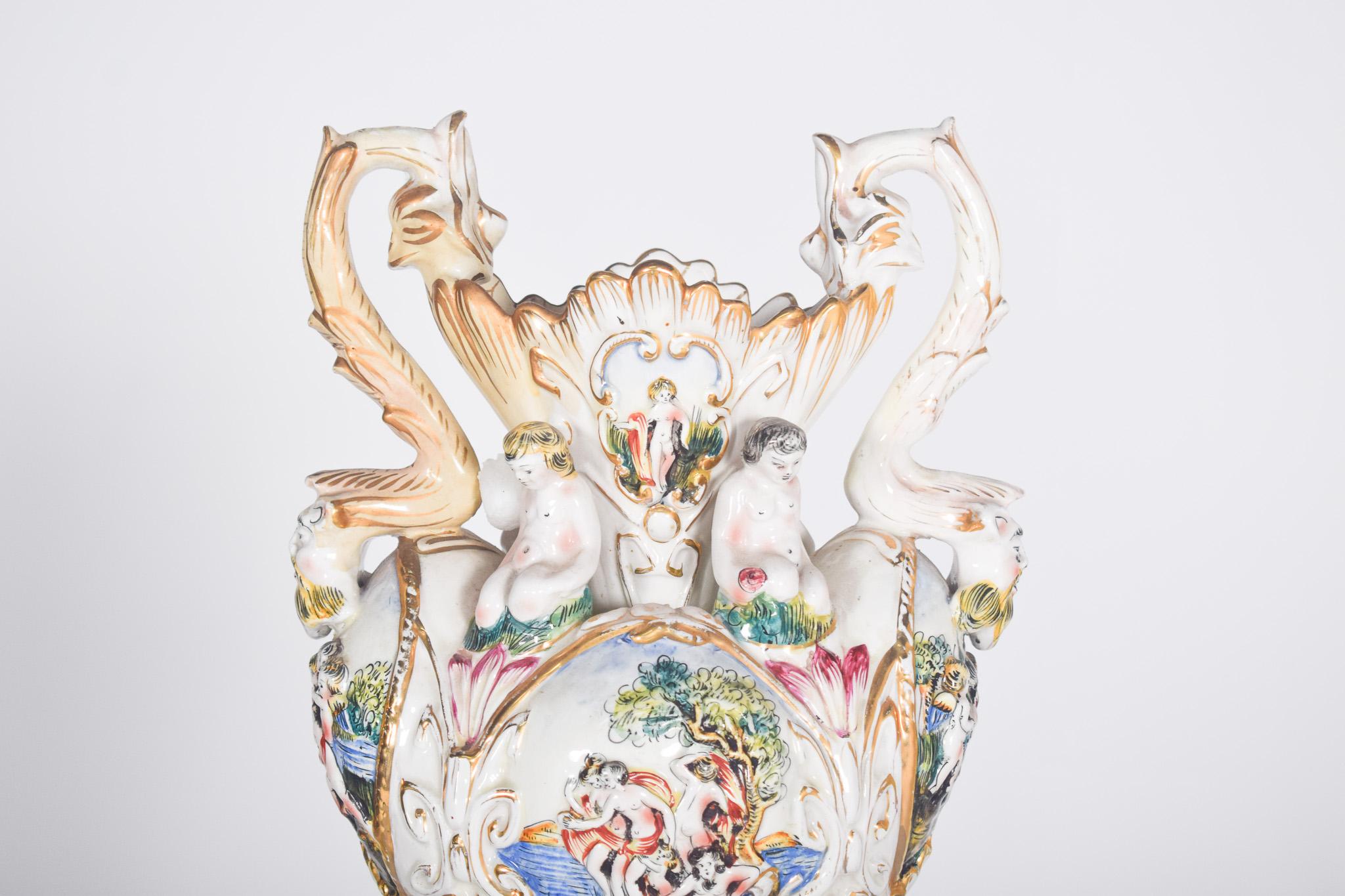 Vaso di ceramica a forma di Amphora. Decorazioni policrome e dorate lavorate a rilievo con foglie e altri ornamenti. Rappresenta un medaglione con figure che riposano sotto un albero sulla riva del fiume, sormontato da ragazzi che riposano sulle
