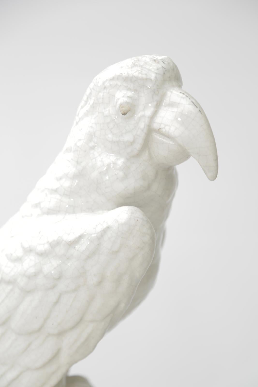 A well-articulated pottery sculpture of a parrot perched upon a tree branch, the body of the parrot is cast in glazed porcelain, while the bottom remains bisque. raised on a ceramic plinth. 

Stock ID: D3231.