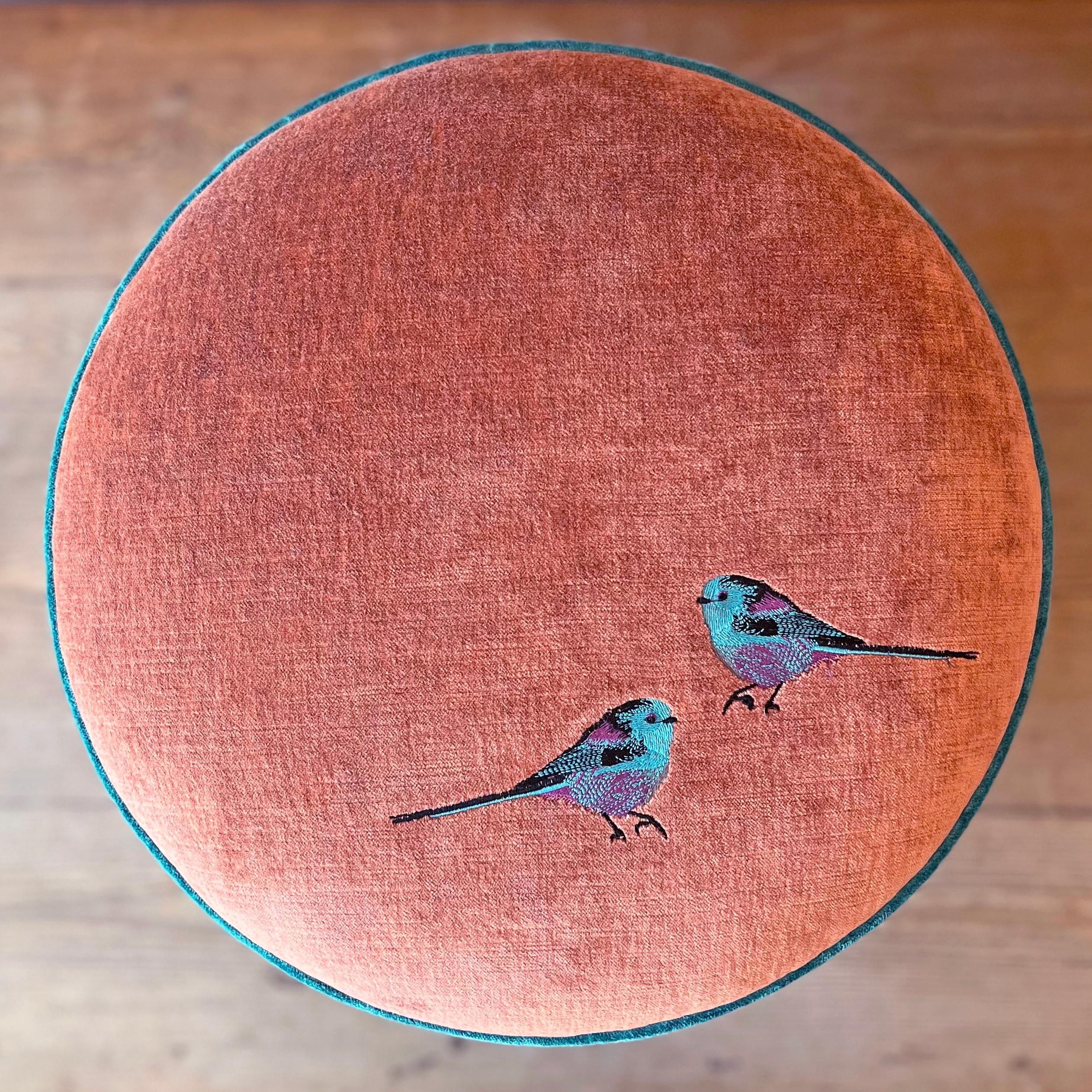 Ein Hocker wie ein kleines häusliches Juwel: Rosa, Violett und ein blauer Akzent verflechten sich in einer Palette von Eleganz und Handwerkskunst, verziert mit einer sorgfältigen Handstickerei von zwei farbigen Rotkehlchen.
Das Design besteht aus