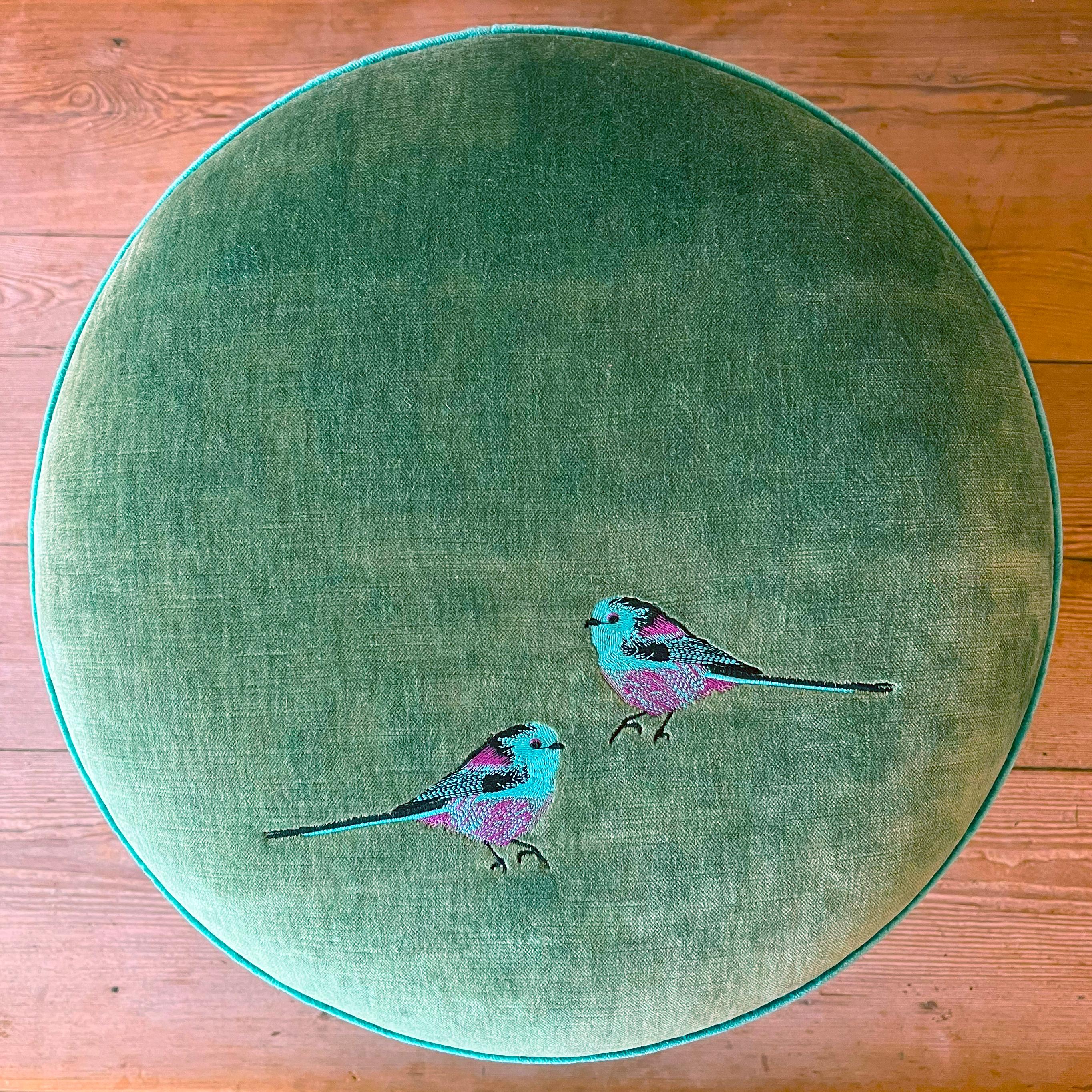 Un pouf come un piccolo gioiello domestico: verde acqua, viola e un accento di azzurro si intrecciano in una palette all’insegna dell’eleganza e dell’artigianalità, impreziosita da un minuzioso ricamo manuale di due pettirossi colorati.
Il design è