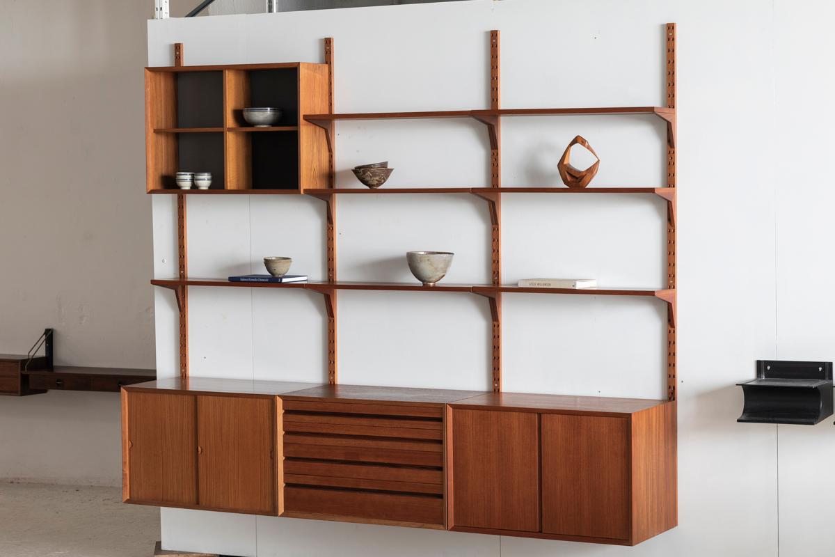 Three-piece wall unit designed by Poul Cadovius and produced by Cado in Denmark around 1960. This shelving system in teak is part of the luxurious Cado series, with wooden dowel supports. It features 7 shelves of 22cm, an open display cabinet and 3