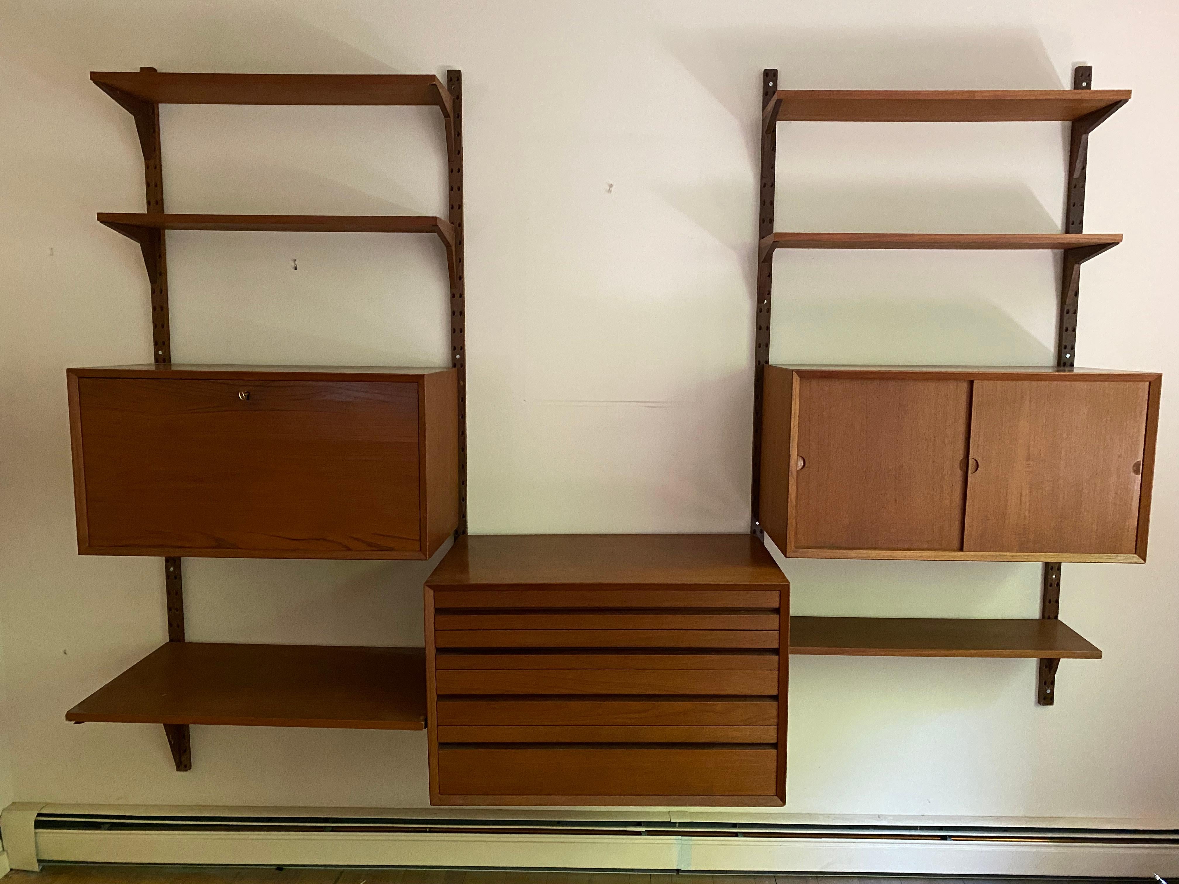 Three bay mahogany Poul Cadovius Cado wall unit. Made in Denmark. The three cabinets consist of a four drawer cabinet, a sliding door cabinet with an adjustable shelf and a drop down cabinet with cubbies and shelves that locks (with key). Eight