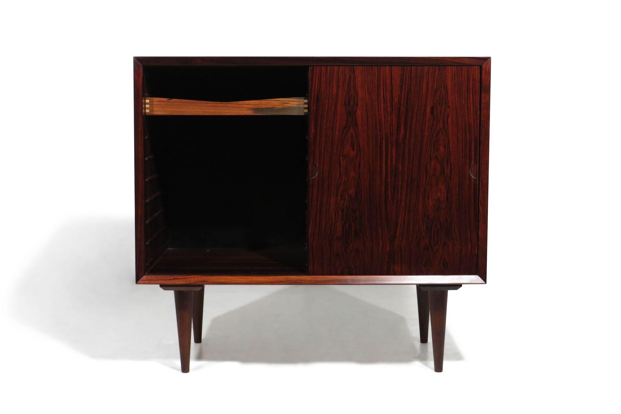 Poul Cadovius Rosewood cabinet with book-matched sliding doors revealing an interior of mahogany with adjustable shelves and small drawer. Minimal design with mitered corners and hand-carved inset pulls. Raised on tapered legs. Perfect as a bedside