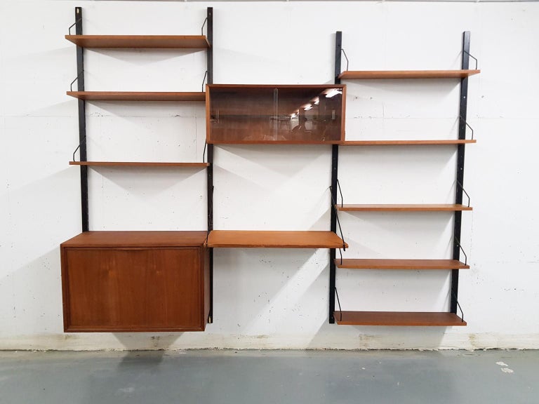Large wall unit by Poul Cadovius for Royal system. With 4 wooden risers and teak veneer shelves and cabinets.

1x cabinet 52 x 40 x 80 cm ( HxDxW)
1x Cabinet with glasss doors 34 x 28 x 80 cm ( HxDxW)
1 x desk shelf 48 x 80 cm (DxW)
3 x shelf