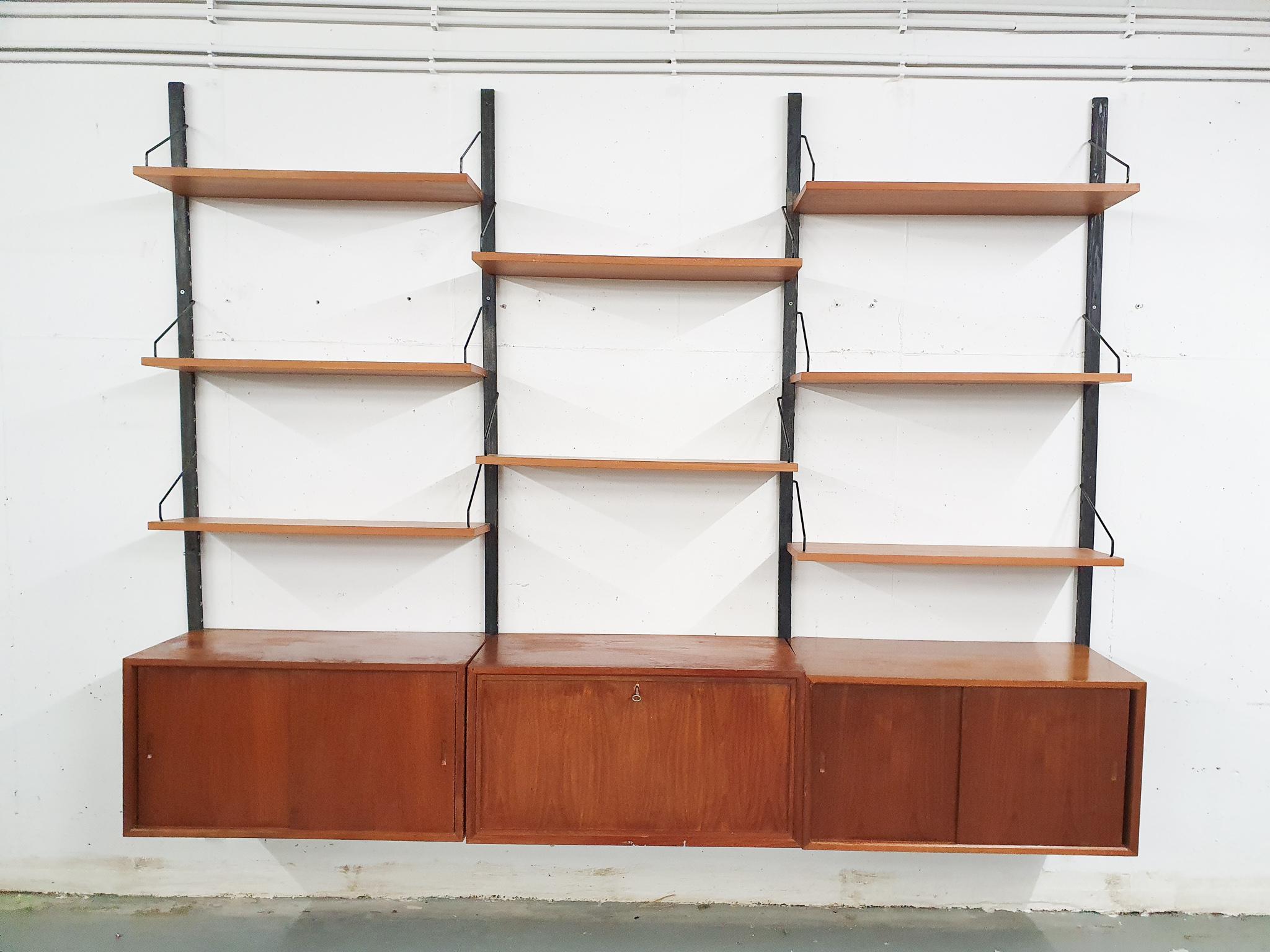 Wall unit with four black teak risers, three cabinets and eight shelves. Designed by Poul Cadovius for Royal System.
The system has no large damages, but has traces of use consistent with age and use. The risers are not original, but custom made by