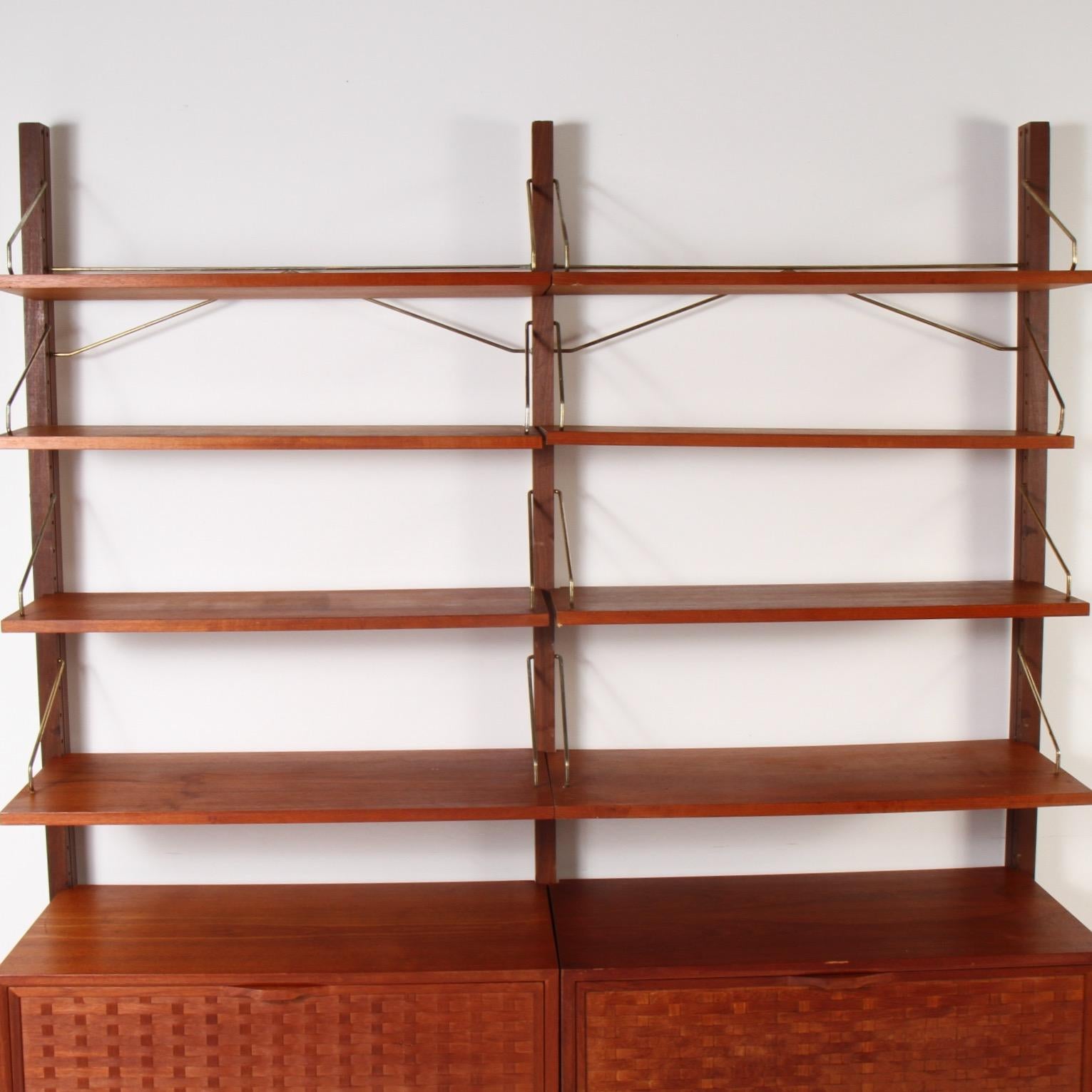 Two column teak Cado wall system that features 8 adjustable teak shelves and two drop down basket-weave cabinets.