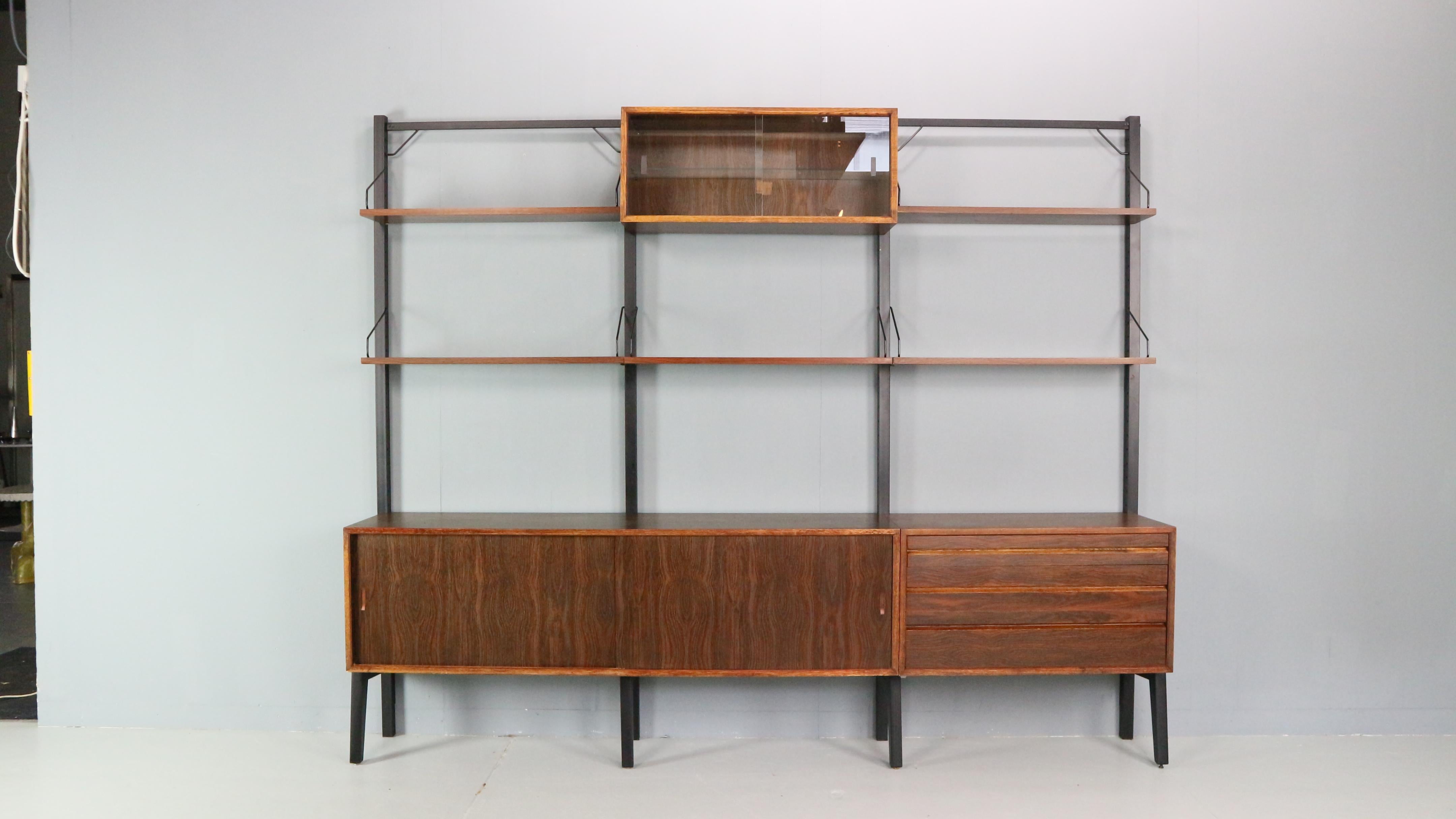 Original freestanding wall unit designed by Poul Cadovius, model Royal, in the 1960s for Royal System, Denmark.
Freestanding wall unit in dark wood, consists 4  black metal standers, five shelves, one glass cabinet, one cabinet with drawers and a